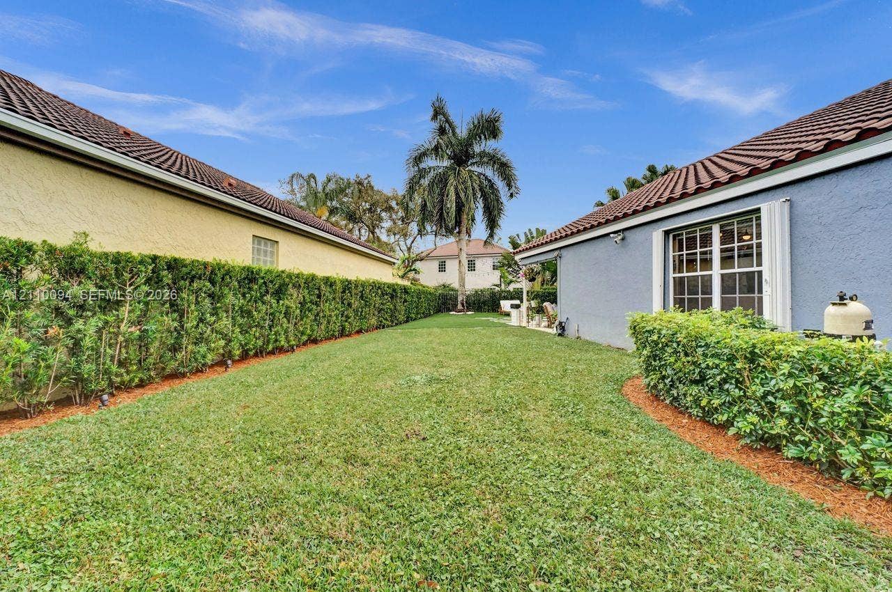2064 Island Circle, Weston, FL 33326 Private outdoor space featuring manicured lawn, established perimeter hedges, and a mature palm tree
