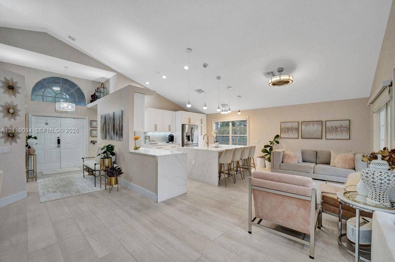 2064 Island Circle, Weston, FL 33326 Open-concept interior featuring vaulted ceilings, a central kitchen island with waterfall-edge countertop, recessed lighting, and wood-finish flooring