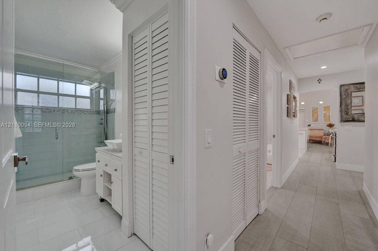 2064 Island Circle, Weston, FL 33326 Bathroom featuring a glass-enclosed shower, vessel sink vanity, and white tile flooring, with dual louvered-door closets and wood-finish flooring in the hallway