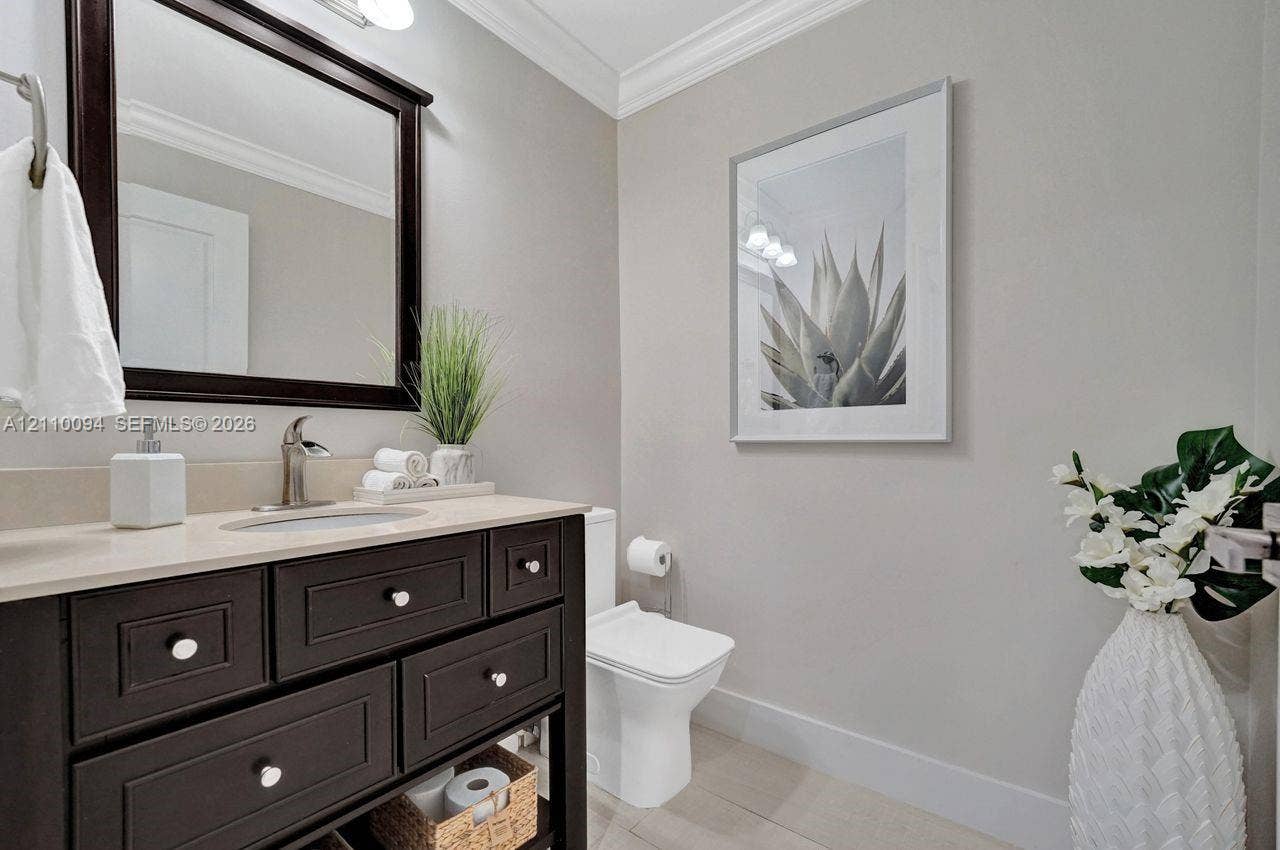 2064 Island Circle, Weston, FL 33326 Dark-finish vanity featuring an integrated basin and light-toned countertop, framed wall mirror, and crown molding