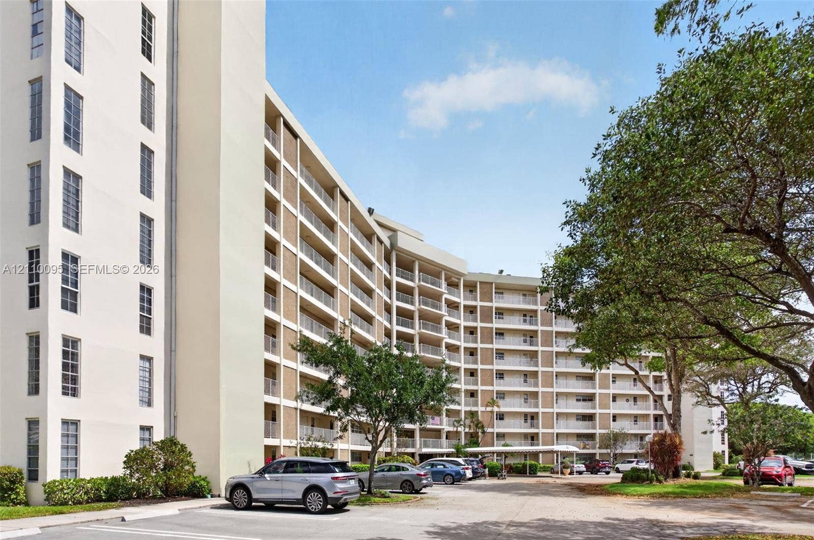 3090 N Course Drive, #807, Pompano Beach, Pompano Beach, FL 33069 Multi-story residential building exterior featuring stacked balconies, exterior corridor lighting, and a paved parking area with covered parking structures