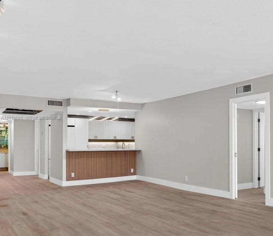 3090 N Course Drive, #807, Pompano Beach, Pompano Beach, FL 33069 Open-concept interior featuring wood-finish flooring, a kitchen peninsula with vertical slat detailing, white cabinetry, and modern integrated pendant lighting