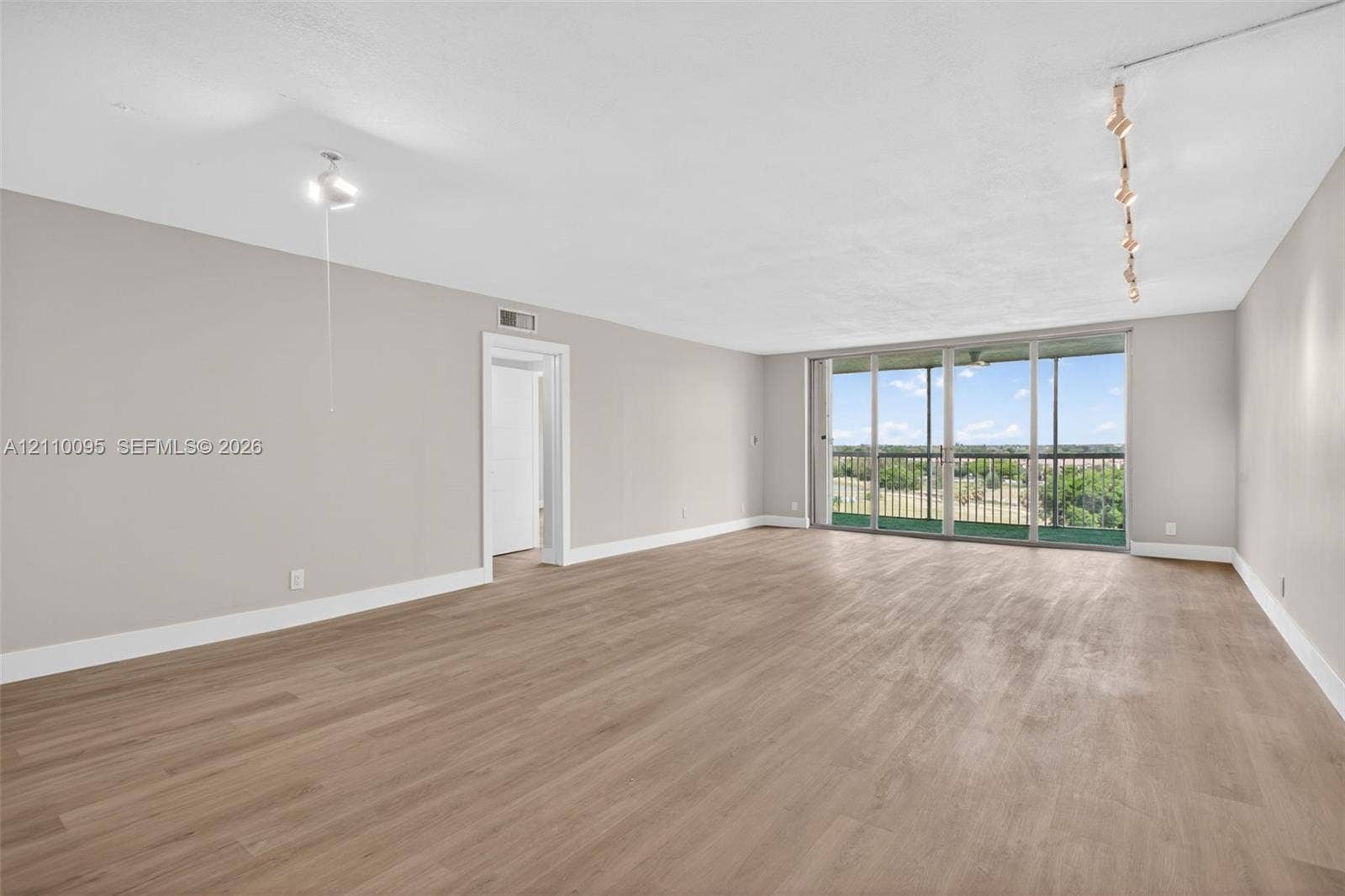 3090 N Course Drive, #807, Pompano Beach, Pompano Beach, FL 33069 Expansive living area featuring light-toned wood-finish flooring, floor-to-ceiling glass sliding doors, a covered balcony, and adjustable track lighting