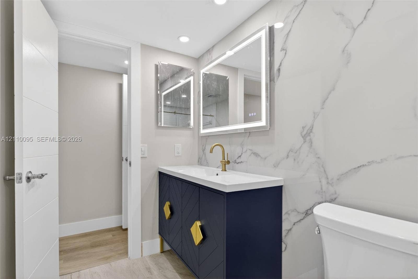 3090 N Course Drive, #807, Pompano Beach, Pompano Beach, FL 33069 Navy blue vanity with geometric door detailing, brass hardware, integrated sink, large-format stone-look wall cladding, and a rectangular LED-backlit mirror