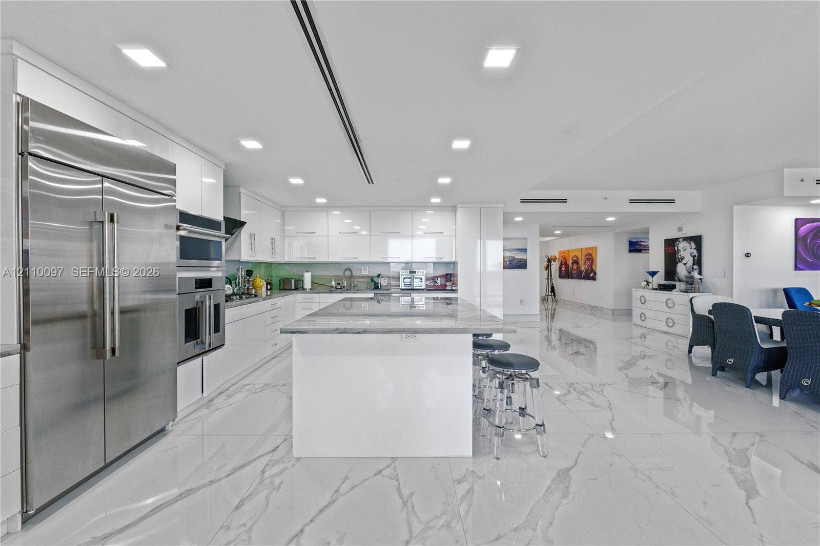 Contemporary kitchen featuring high-gloss cabinetry, a spacious central island with a stone countertop, large-format polished tile flooring, and integrated stainless steel appliances