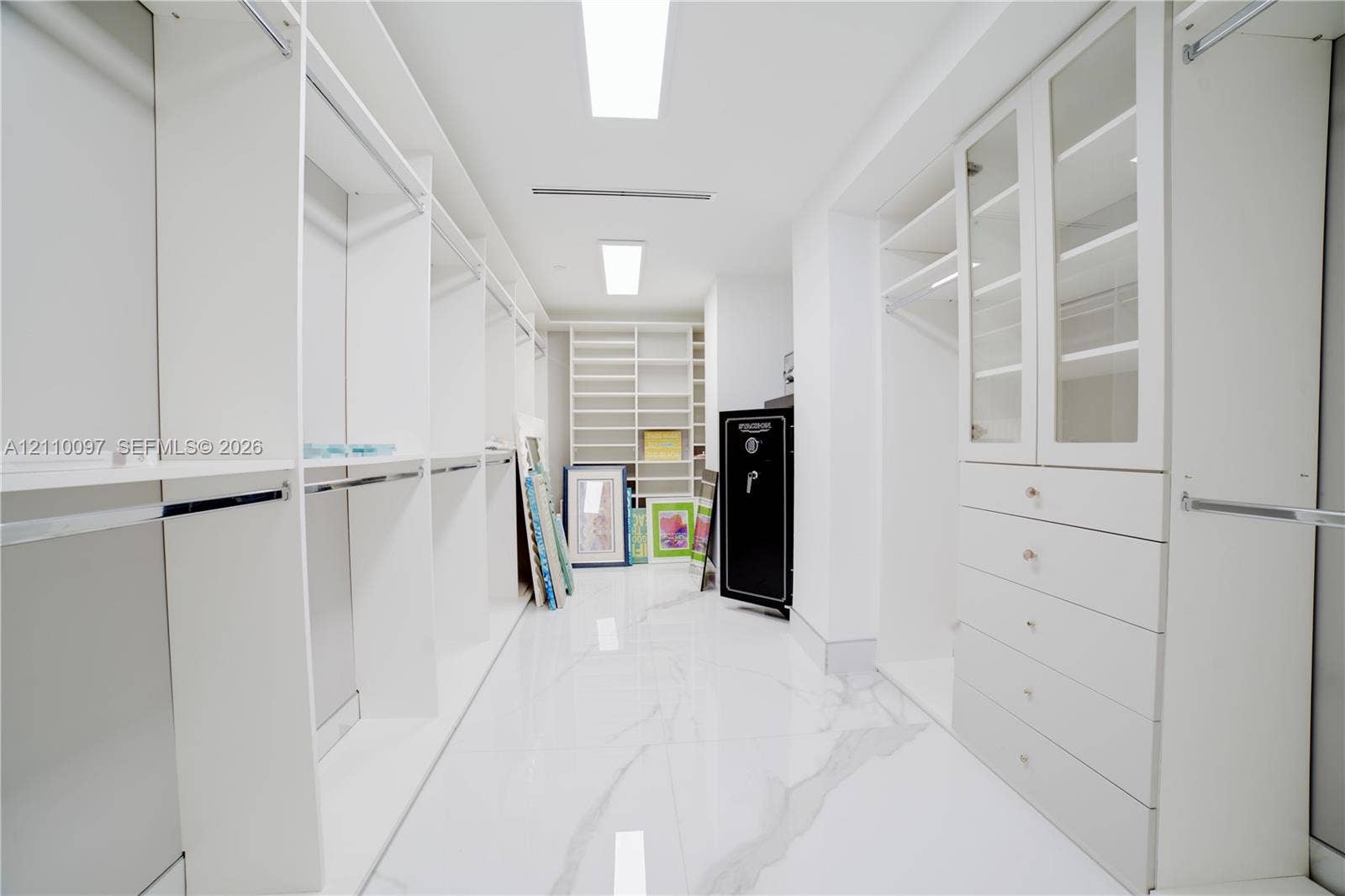 Walk-in closet featuring extensive built-in white cabinetry, glass-fronted upper doors, multiple storage drawers, and polished stone-finish flooring