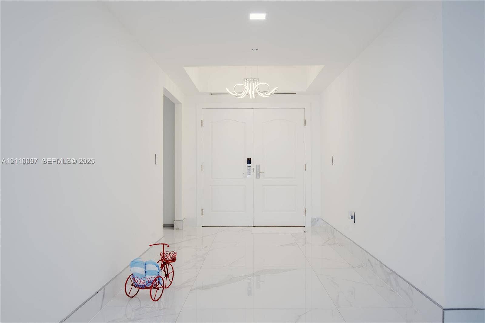 Entryway featuring double doors with a digital lock, large-format stone-patterned flooring, a recessed tray ceiling, and a multi-arm sculptural light fixture