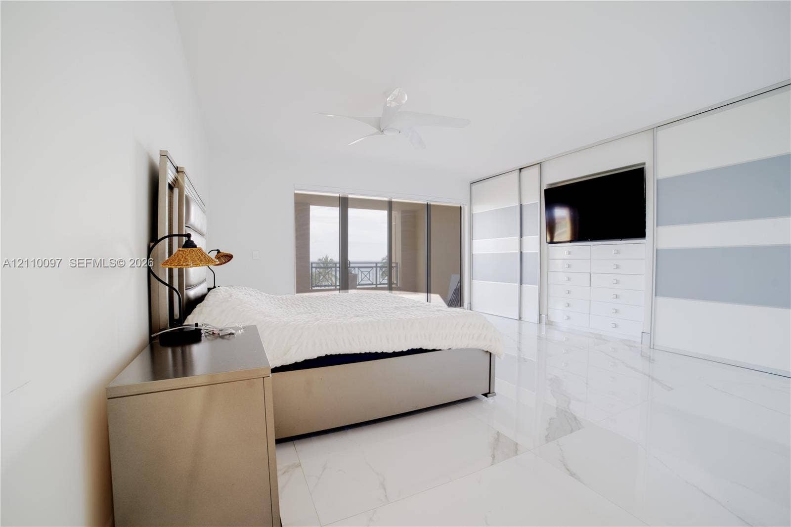 Spacious bedroom featuring polished stone-finish flooring, floor-to-ceiling built-in wardrobe cabinetry, integrated media storage, and a ceiling fan