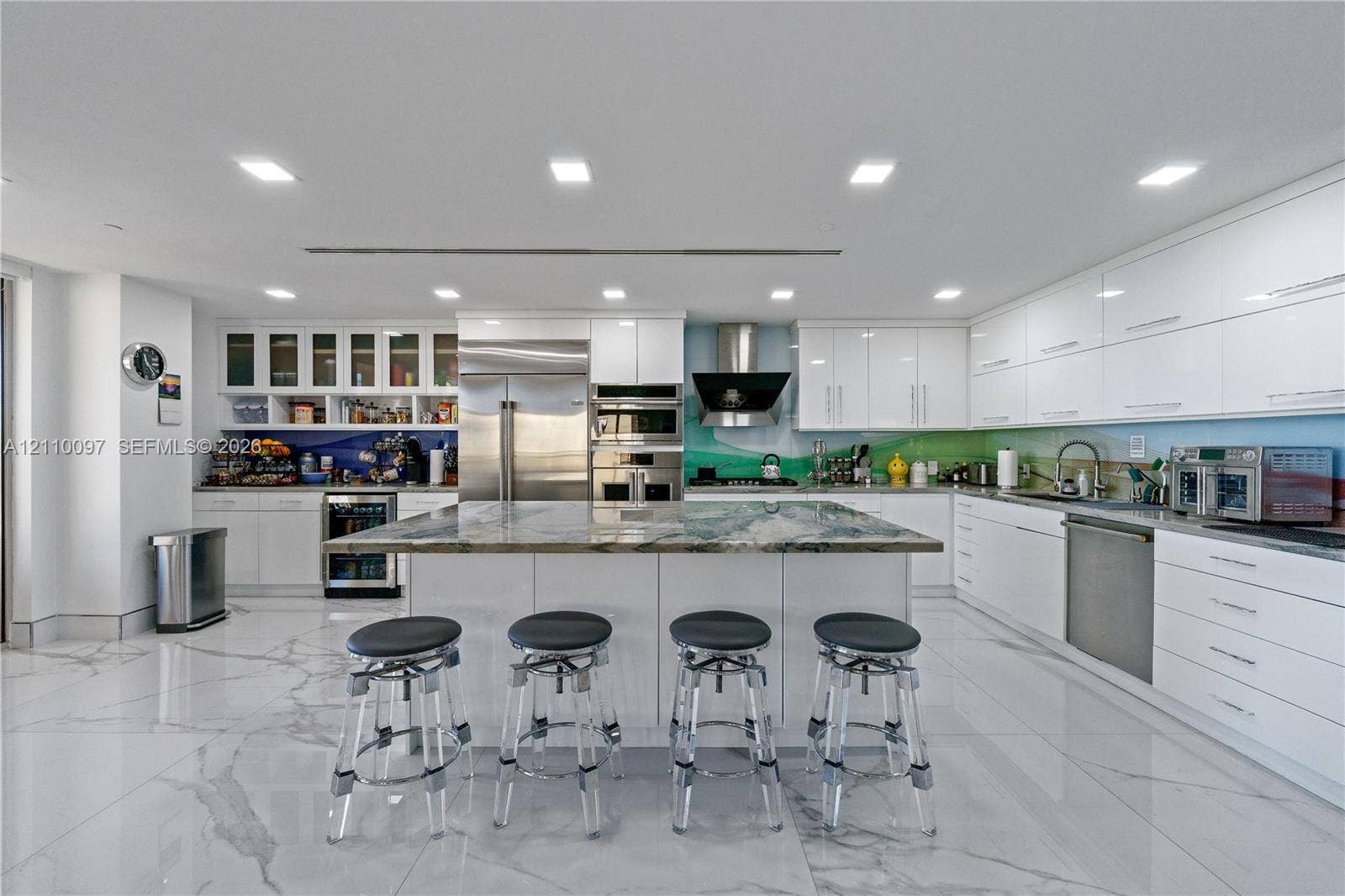 Modern kitchen featuring high-gloss cabinetry, a central island with natural stone countertop, stainless steel appliances, and large-format tile flooring