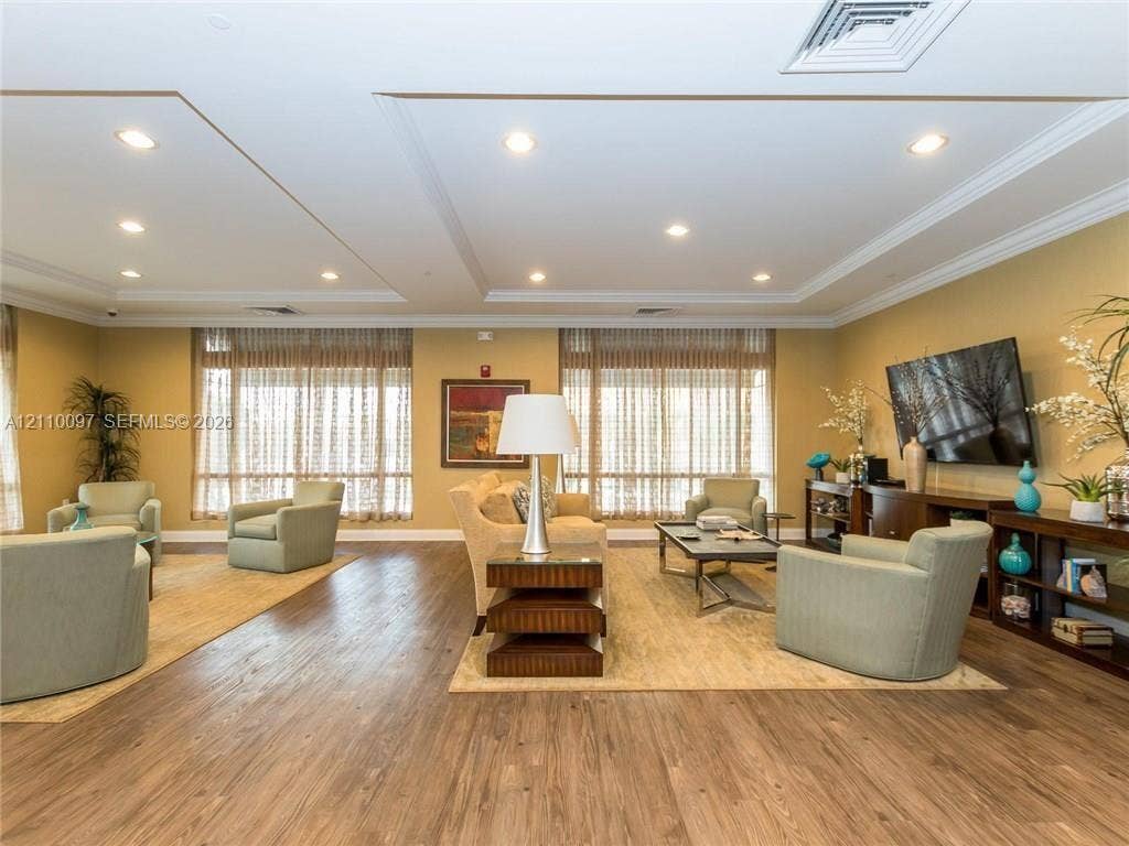 Spacious room featuring wood-finish flooring, recessed lighting, crown molding, and large windows with floor-to-ceiling treatments