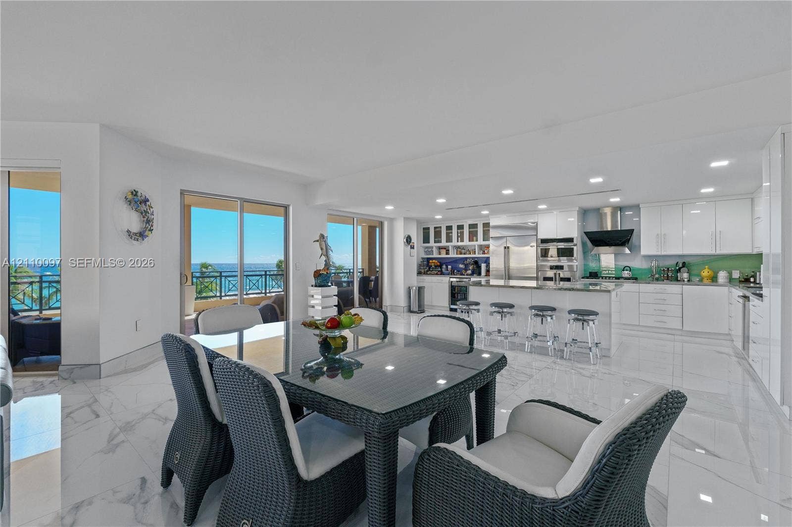 Open-concept space featuring polished stone flooring, recessed lighting, and a kitchen equipped with white cabinetry, built-in stainless steel appliances, and a central island