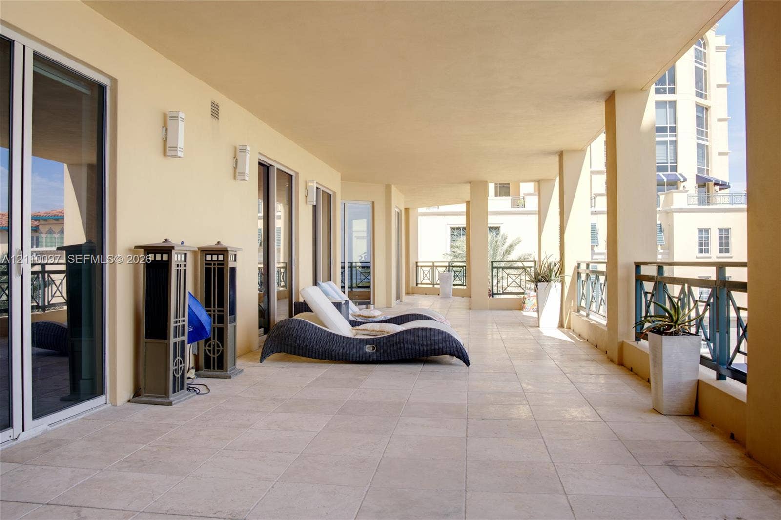 Covered terrace featuring stone tile flooring, structural columns, metal railings, and multiple glass sliding door entrances