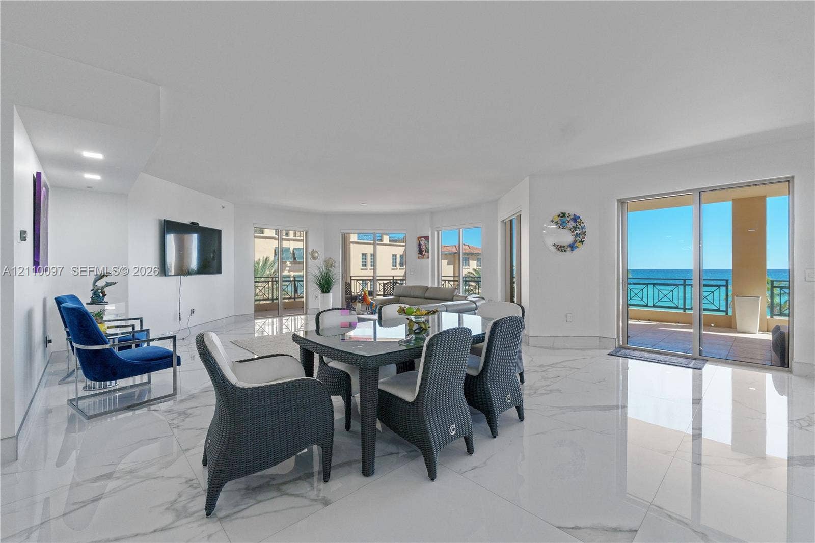 Open-concept living space featuring large-format stone-finish tile flooring, recessed lighting, and multiple sliding glass doors providing access to the exterior balcony with ocean scenery