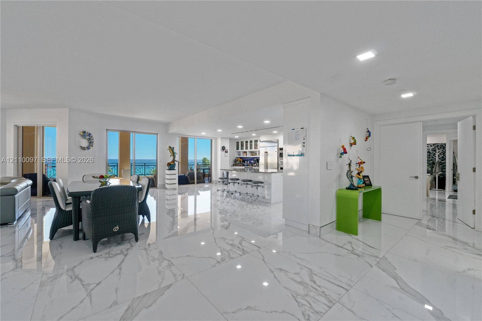Large-format polished stone flooring, recessed ceiling lighting, kitchen island with bar seating, and floor-to-ceiling glass sliding doors