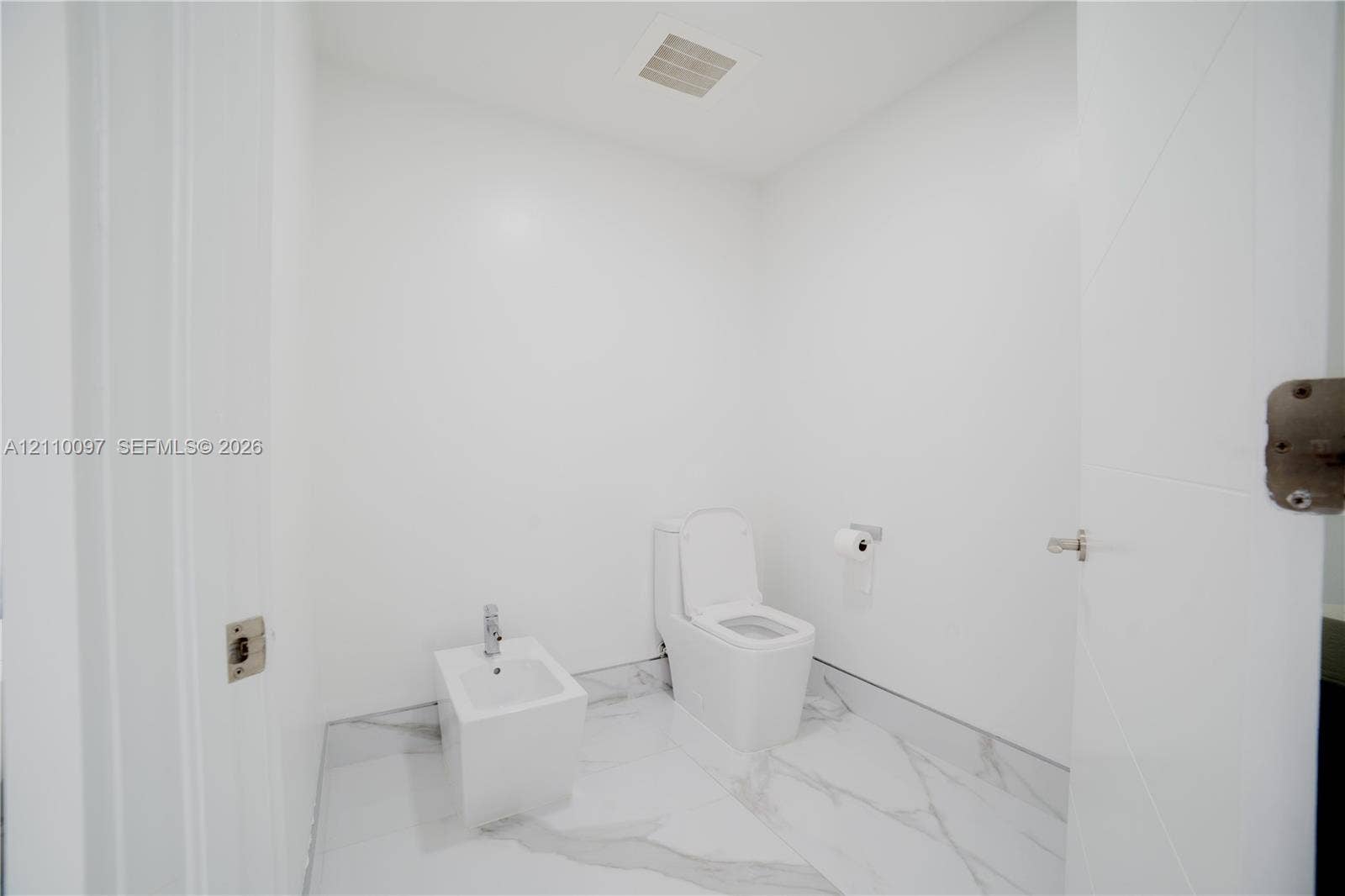 Full-height veined tile flooring, wall-mounted toilet, and bidet with chrome fixtures