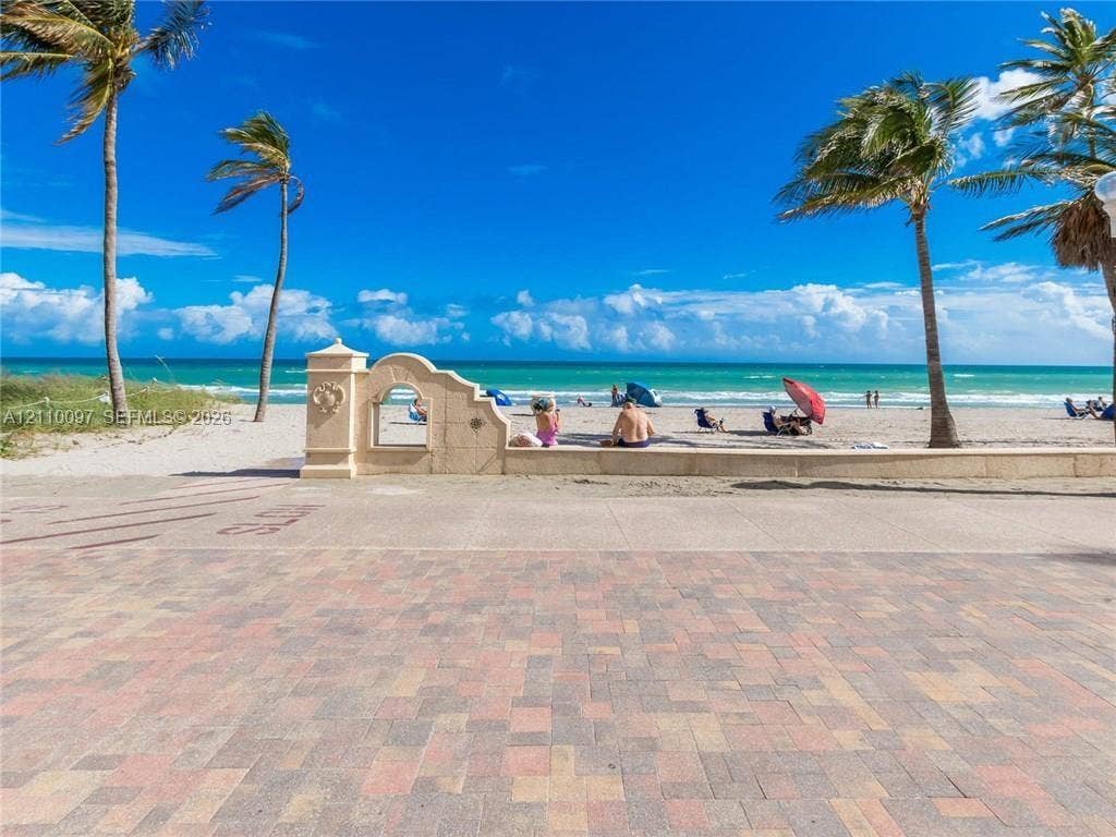 Brick-paver patio featuring a decorative stone archway, perimeter wall, and mature palm trees