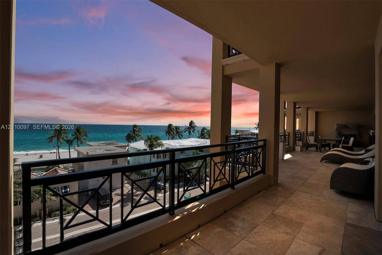 Covered balcony featuring natural stone tile flooring, a geometric metal railing, and expansive ocean and coastal scenery