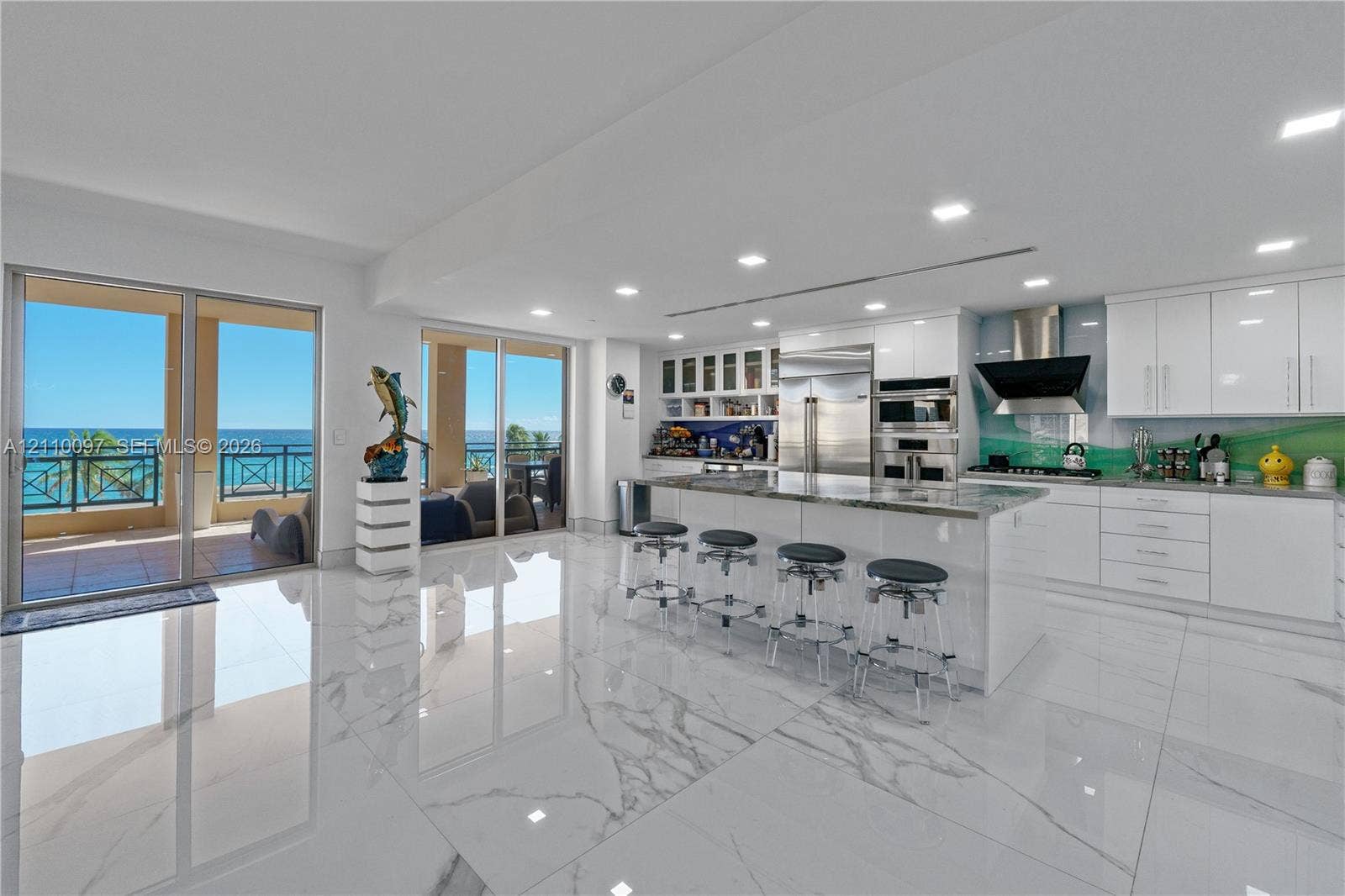 Kitchen featuring glossy cabinetry, a central island with stone countertop, stainless steel appliances, large-format tile flooring, and floor-to-ceiling glass sliding doors