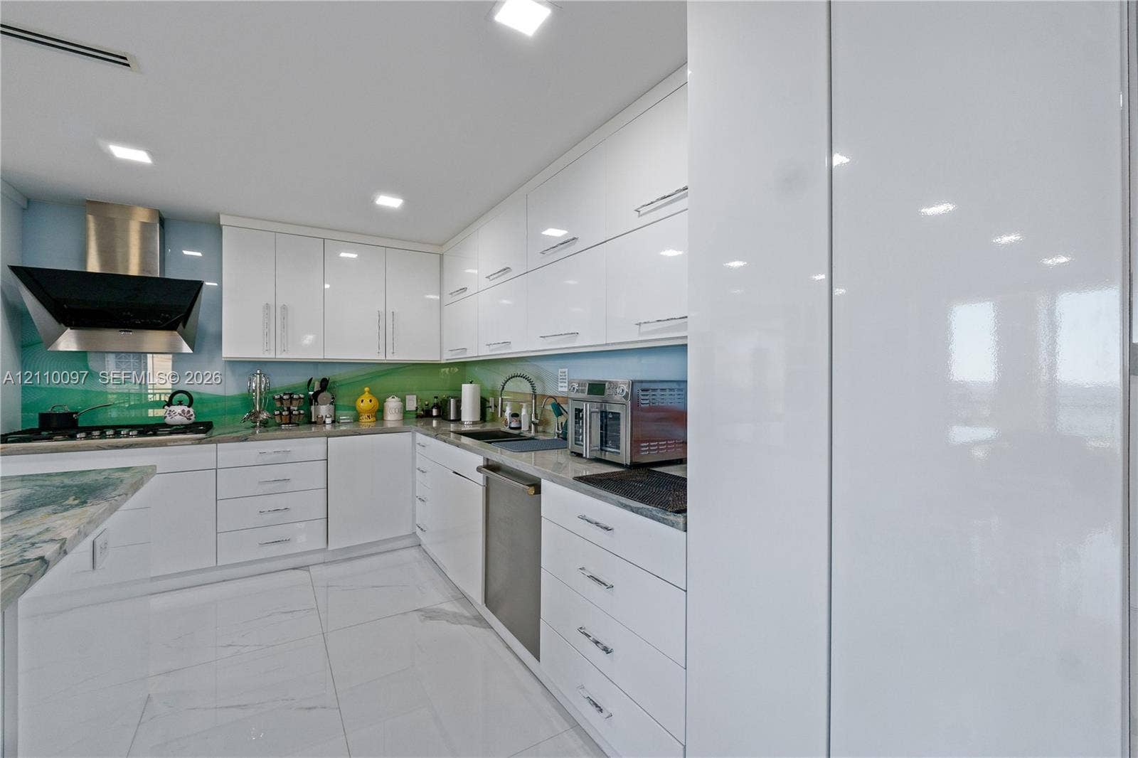 Modern kitchen featuring high-gloss cabinetry, stone countertops, integrated stainless steel appliances, a stainless steel range hood, and large-format tile flooring