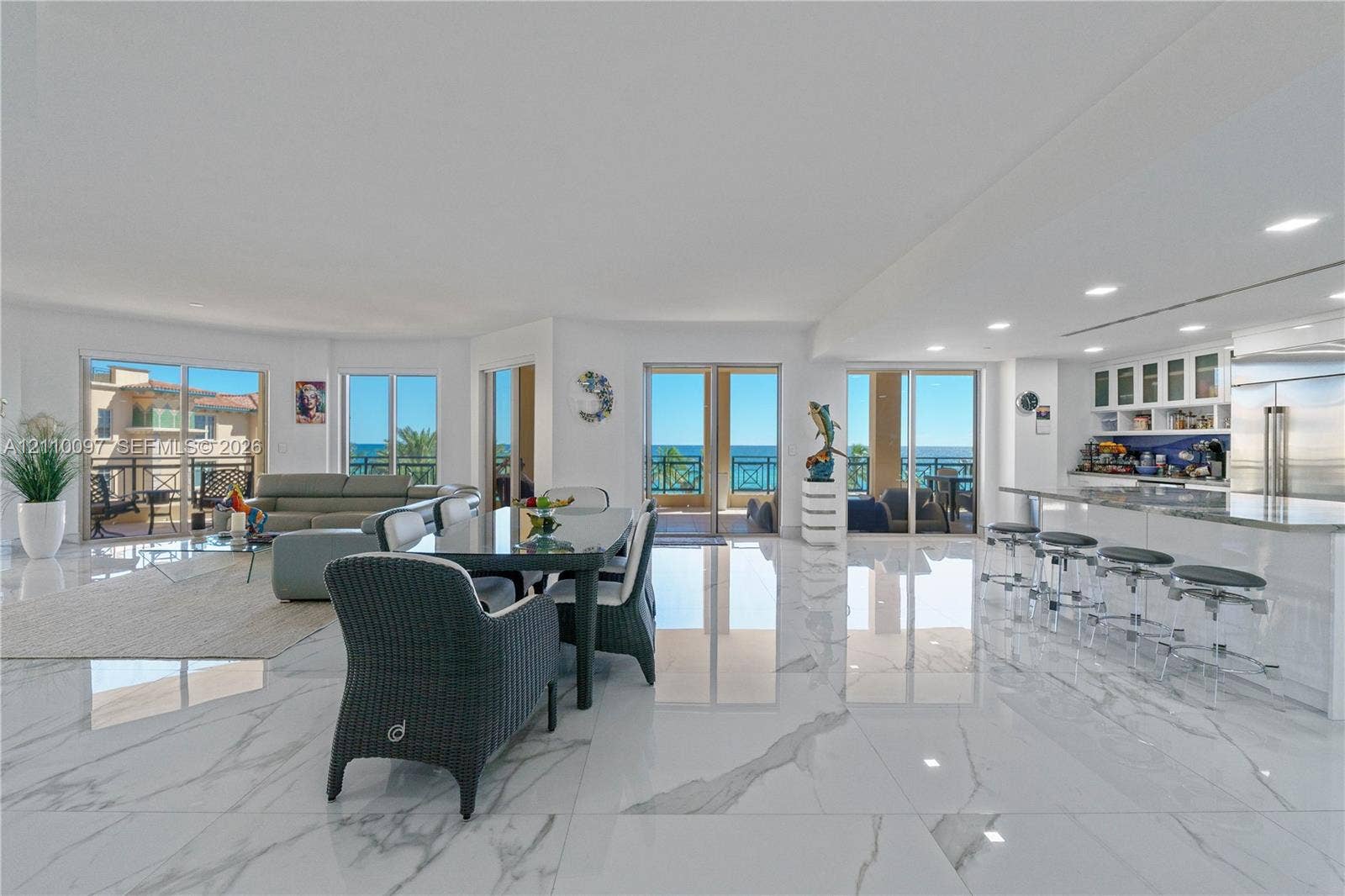 Open-concept living space featuring large-format polished tile flooring, a kitchen island with stone countertop, recessed lighting, and multiple sliding glass doors providing outdoor access