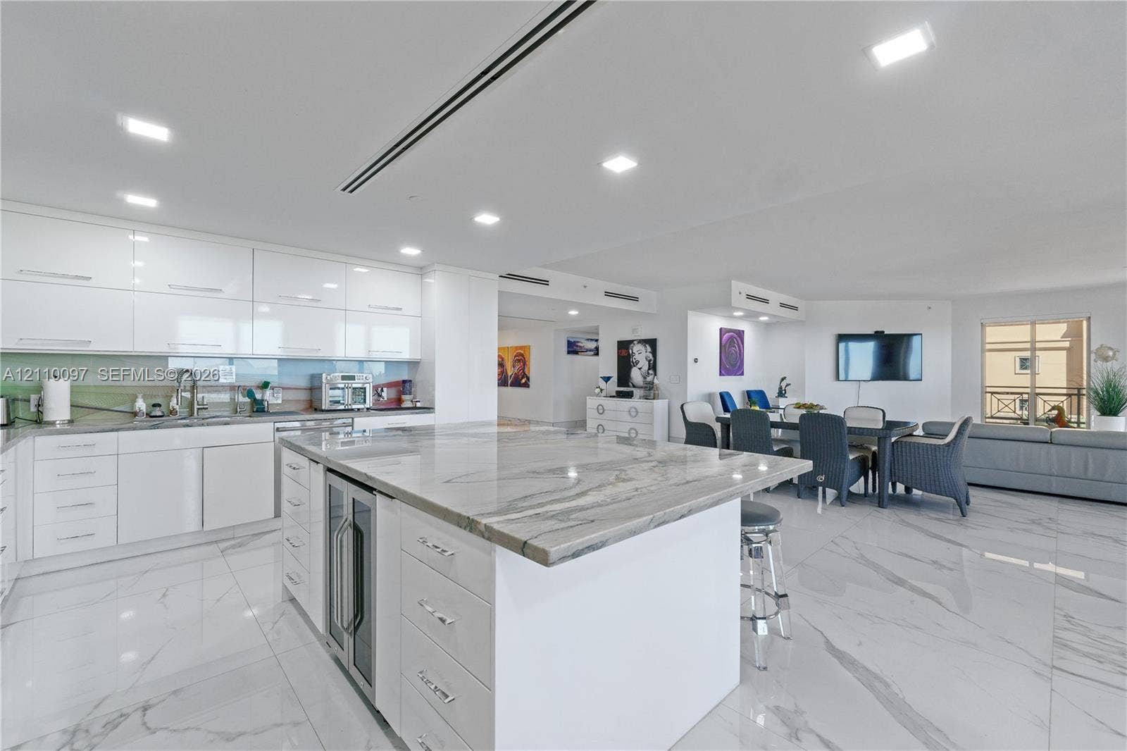 Kitchen featuring high-gloss white cabinetry, stone-finish waterfall island with built-in wine refrigeration, large-format tile flooring, and recessed ceiling lighting