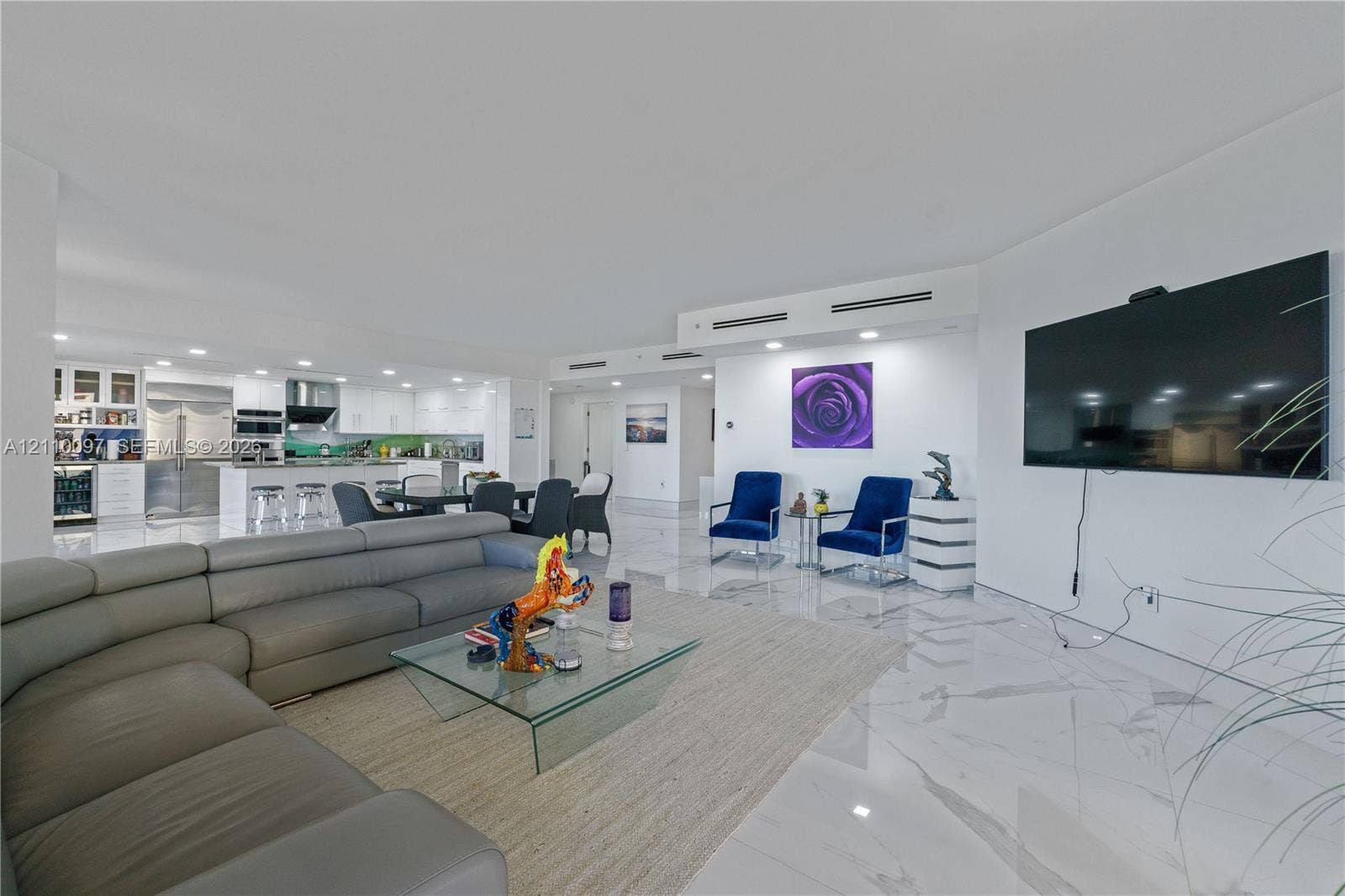 Open-concept living space featuring large-format stone-finish flooring, recessed lighting, white cabinetry, integrated stainless steel appliances, and a kitchen island with a breakfast bar