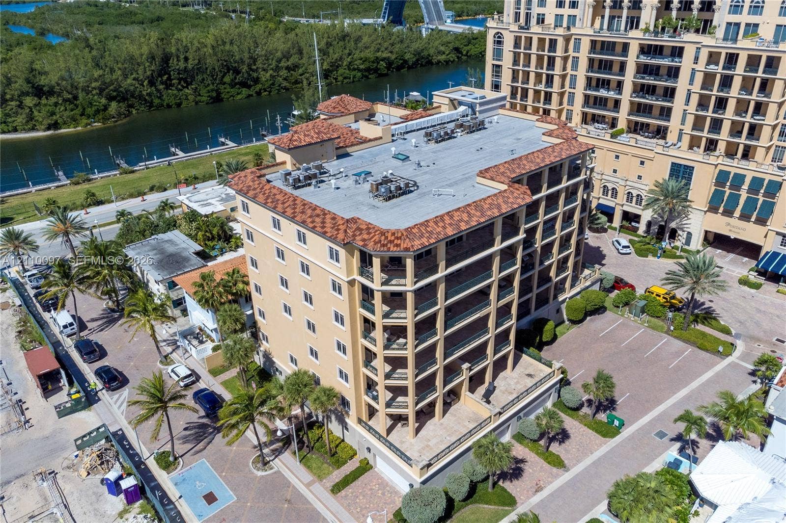 Mid-rise multi-story building featuring tile roofing, covered balconies, beige exterior facade, and paved surface parking
