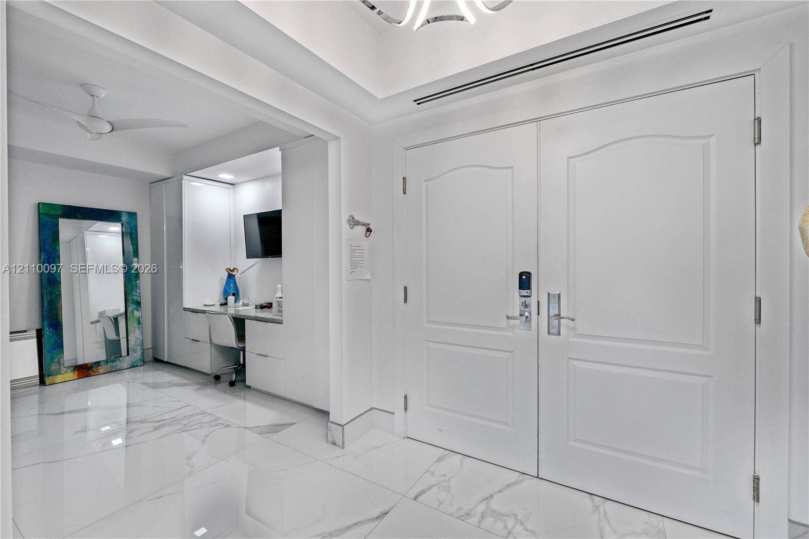 Double entry doors with arch-top panels, large-format tile flooring with marble-finish veining, recessed tray ceiling, and built-in cabinetry featuring integrated workspace