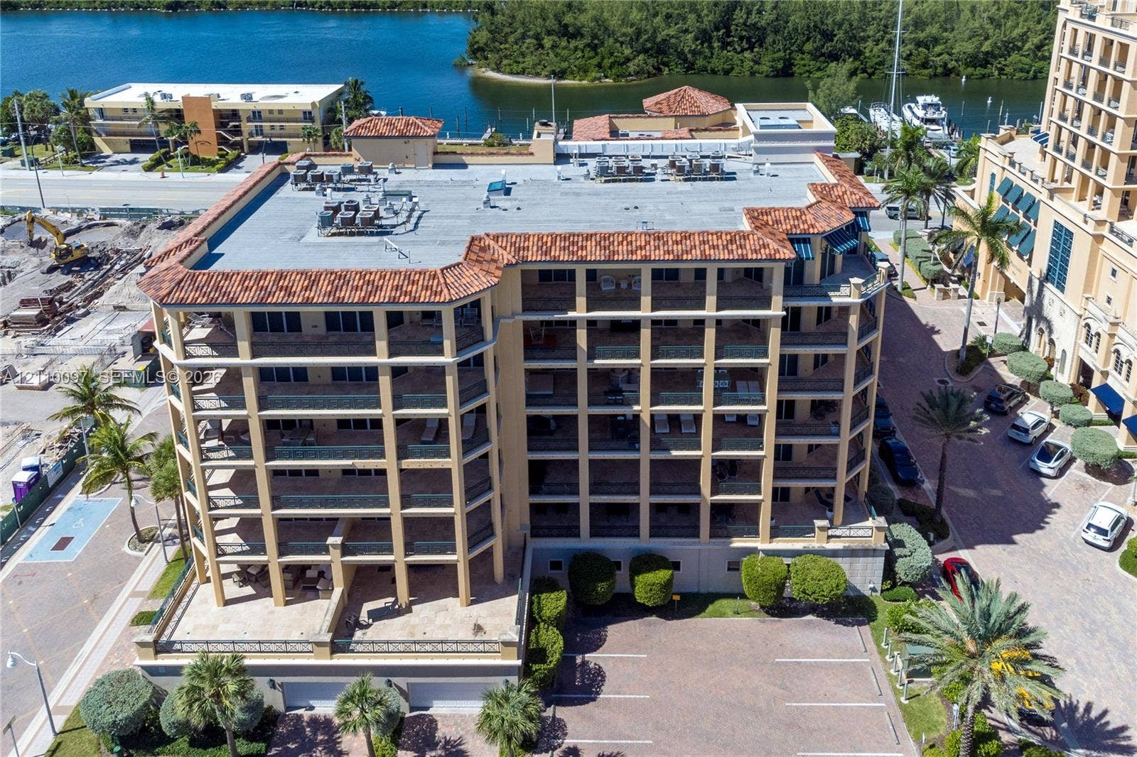 Multi-story building with a terracotta tile roof, structural balconies, paved surface parking, and exterior palm landscaping