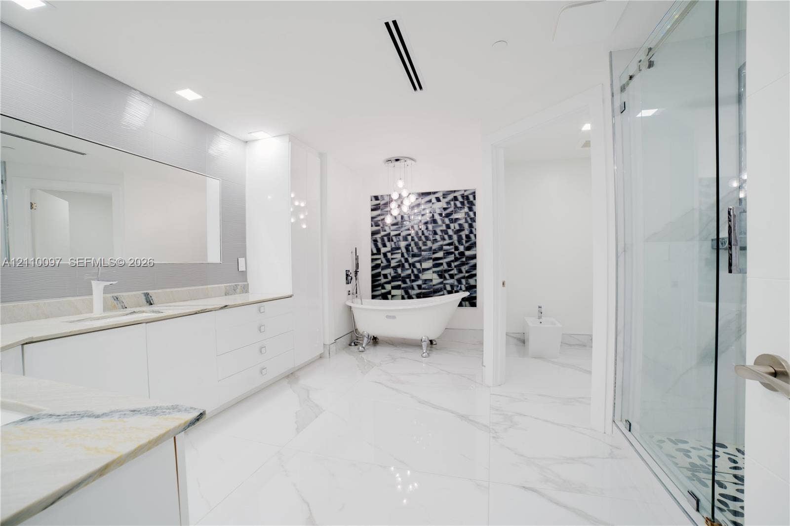Bathroom featuring a claw-foot soaking tub, large format tile flooring with veining, glass-enclosed shower, expansive vanity with integrated sink, and modern pendant lighting