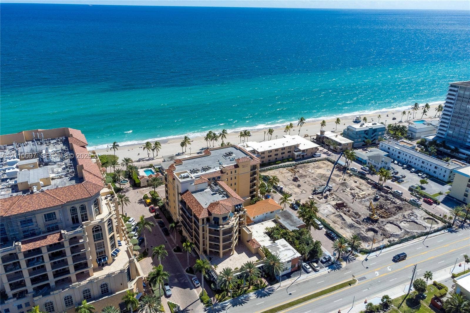 Coastal aerial perspective featuring proximity to the shoreline, multi-story masonry construction, clay tile roofing, and mature palm landscaping