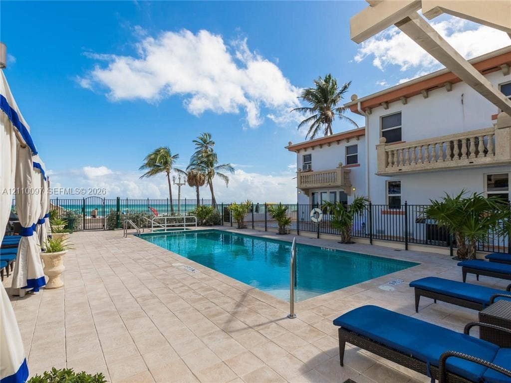 Rectangular swimming pool with tiled surround, wrought iron perimeter fencing, dual second-story balconies with stone-finish balustrades, and multi-level stucco exterior