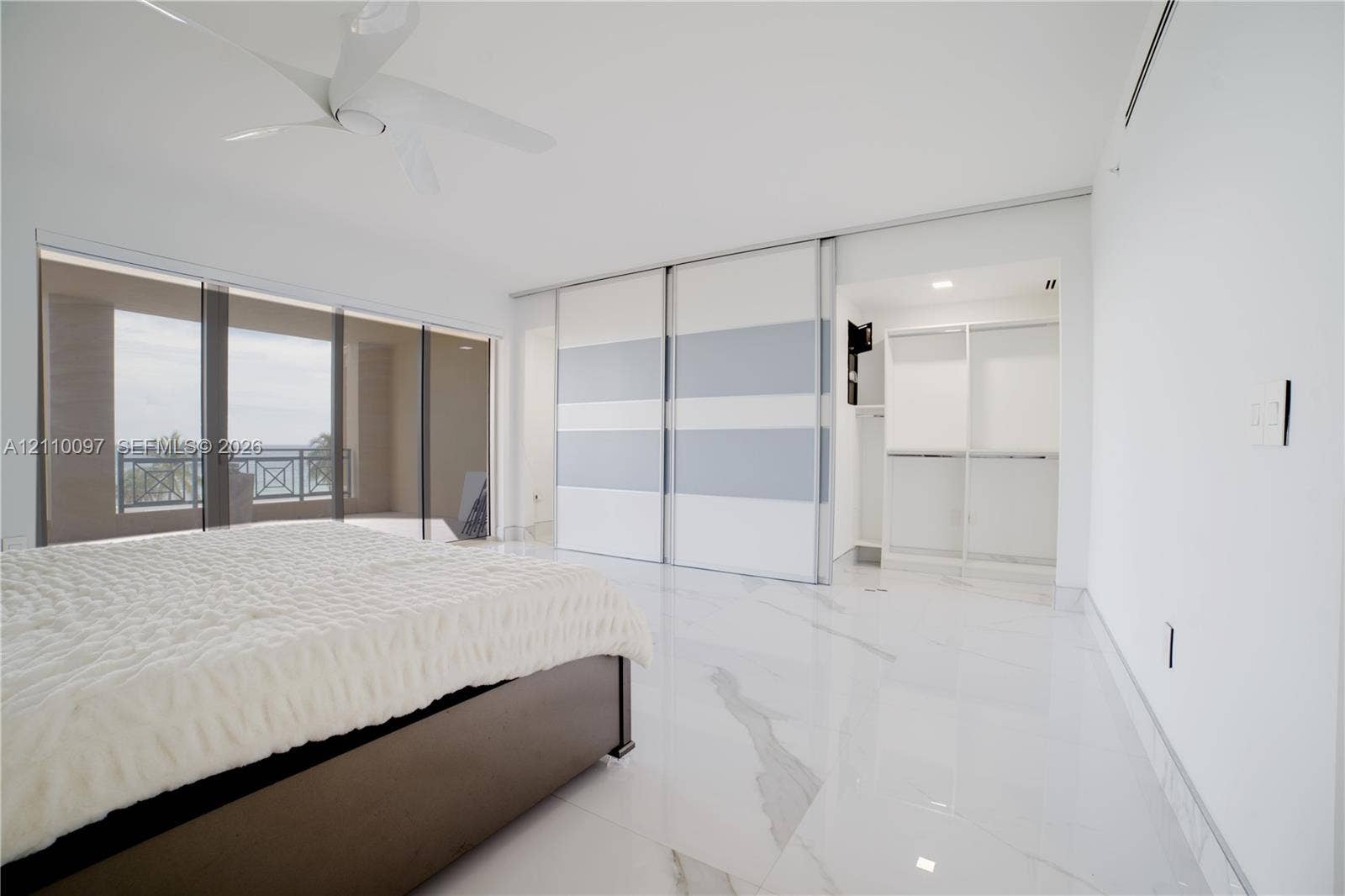 Large-format stone-finish flooring, floor-to-ceiling sliding glass doors, built-in dual-panel sliding wardrobe doors, ceiling-mounted multi-blade fan, and recessed lighting