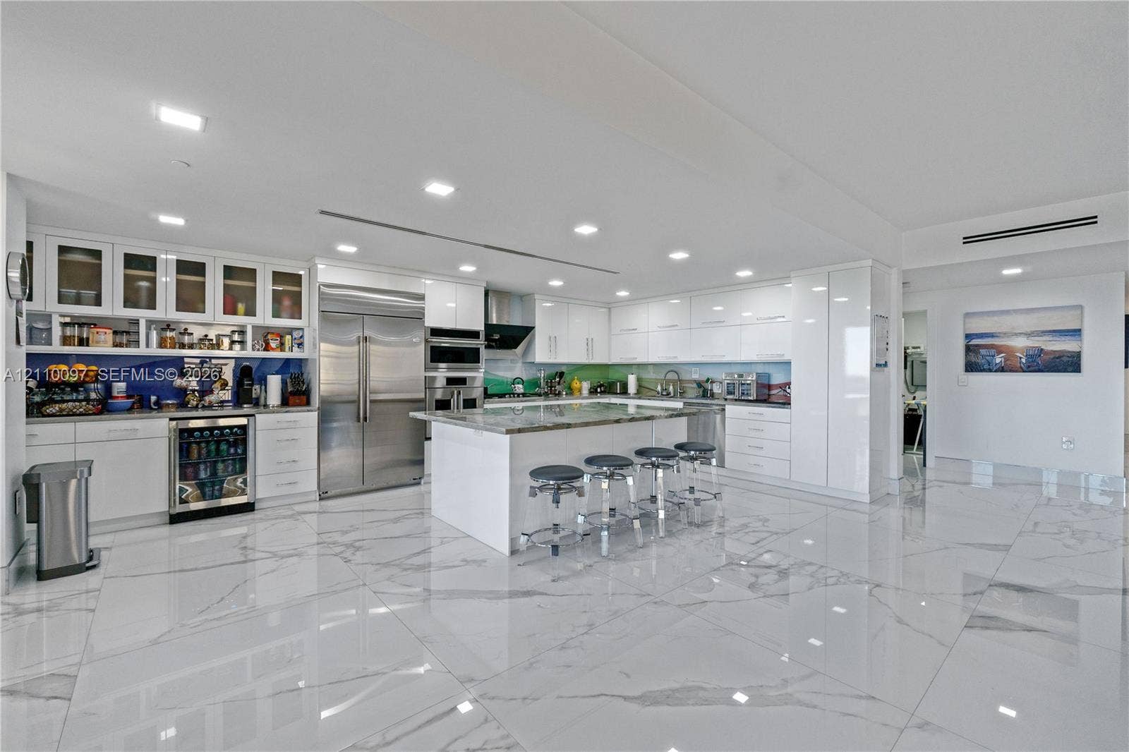Modern kitchen featuring high-gloss white cabinetry, expansive stone-topped center island, large-format polished tile flooring, stainless steel appliances, and integrated wine refrigeration