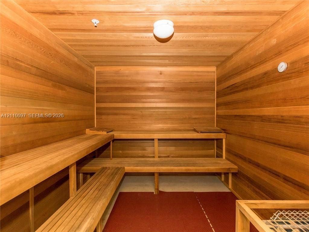 Sauna featuring full wood-paneled walls and ceiling, multi-level built-in wooden benches, and wall-mounted temperature gauge