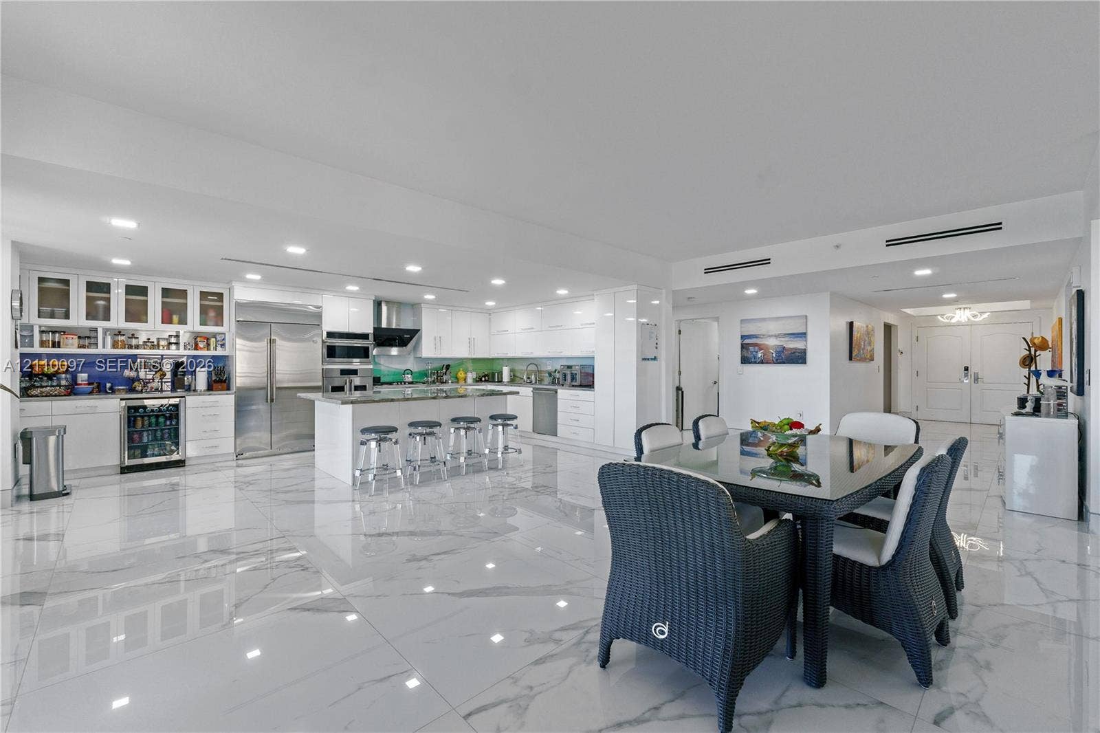 Kitchen featuring white cabinetry, an expansive center island, integrated stainless steel appliances, a beverage refrigerator, and polished stone-finish flooring