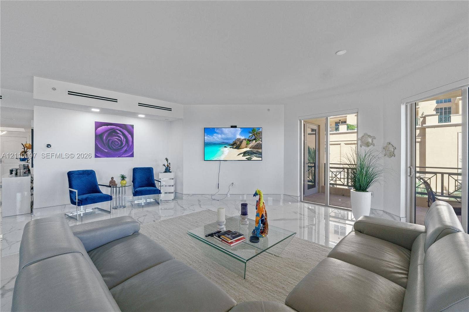 Open-concept interior featuring light-toned stone-finish flooring, recessed linear lighting, and sliding glass doors with balcony access
