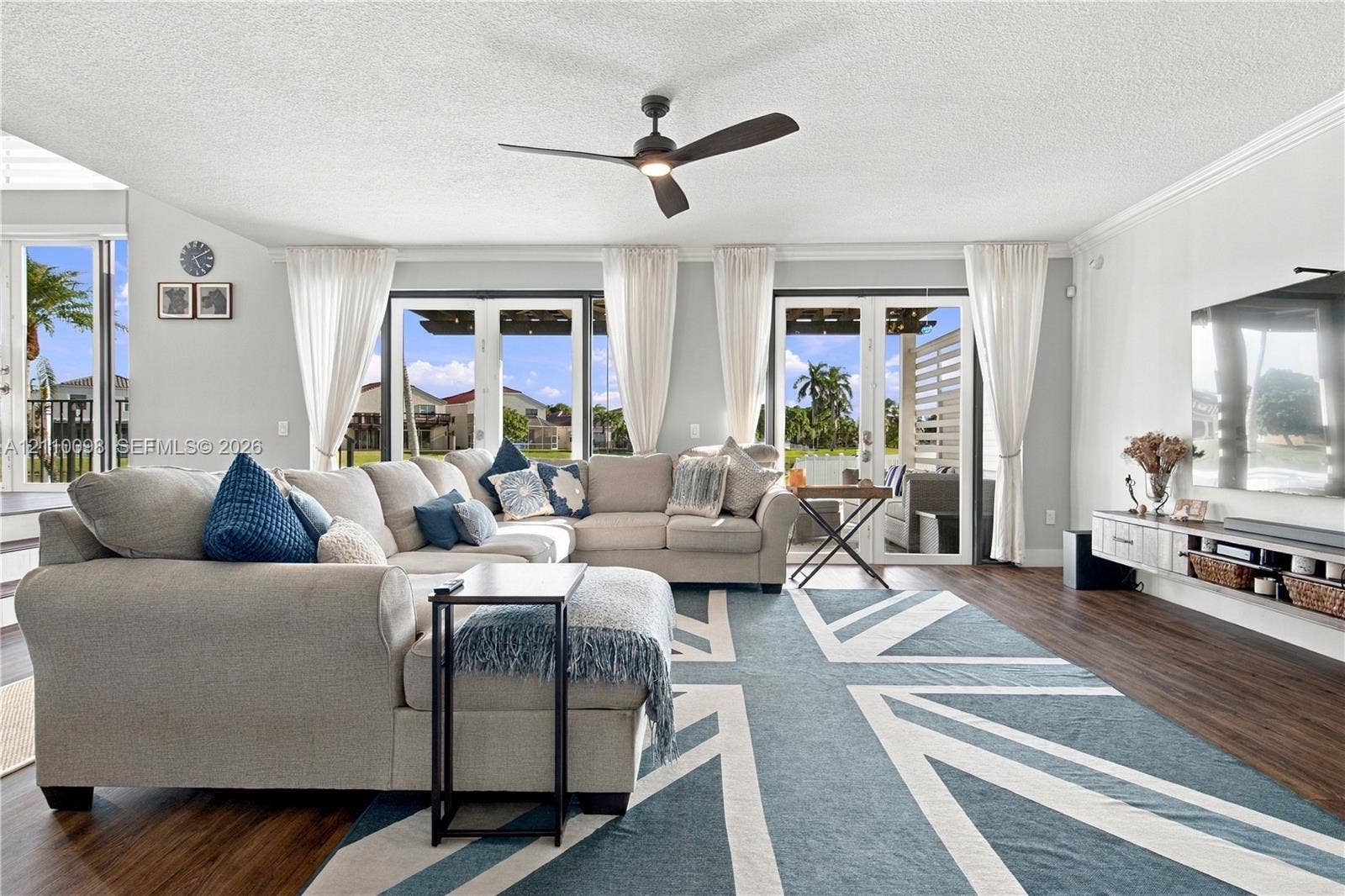 Living area featuring dark wood-finish flooring, dual sets of glass-paneled doors, a modern ceiling fan, and a wall-mounted floating media console