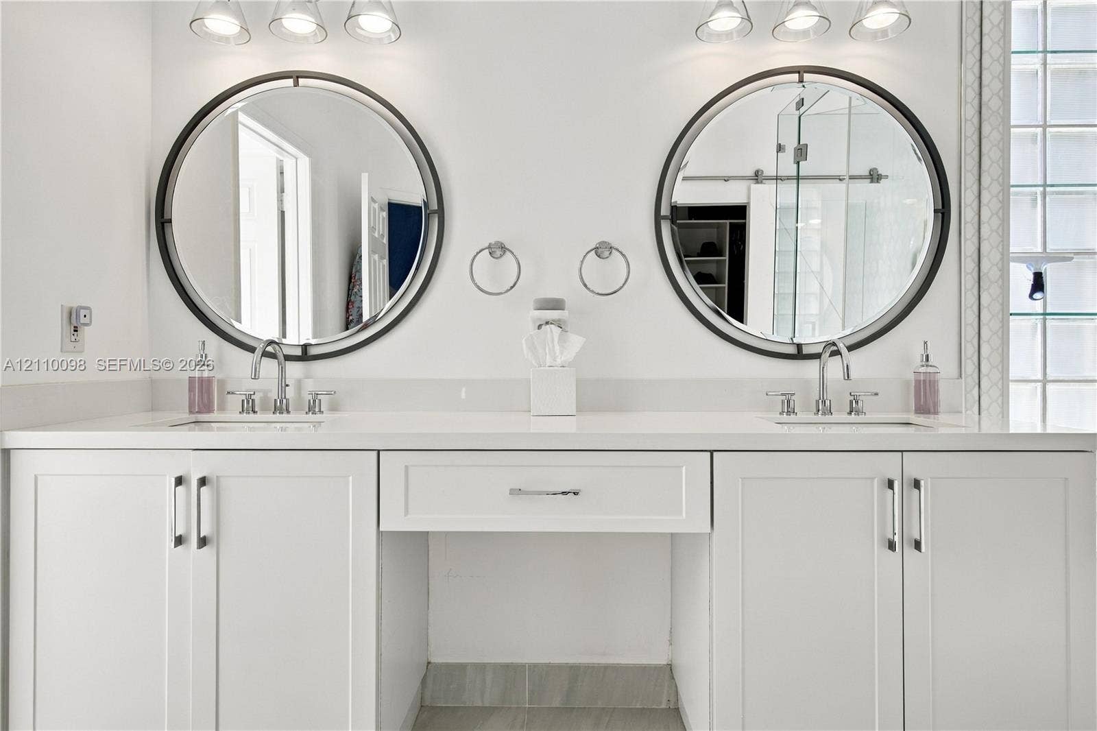Dual-sink vanity featuring white cabinetry, solid surface countertop, two circular mirrors with dark frames, and chrome fixtures