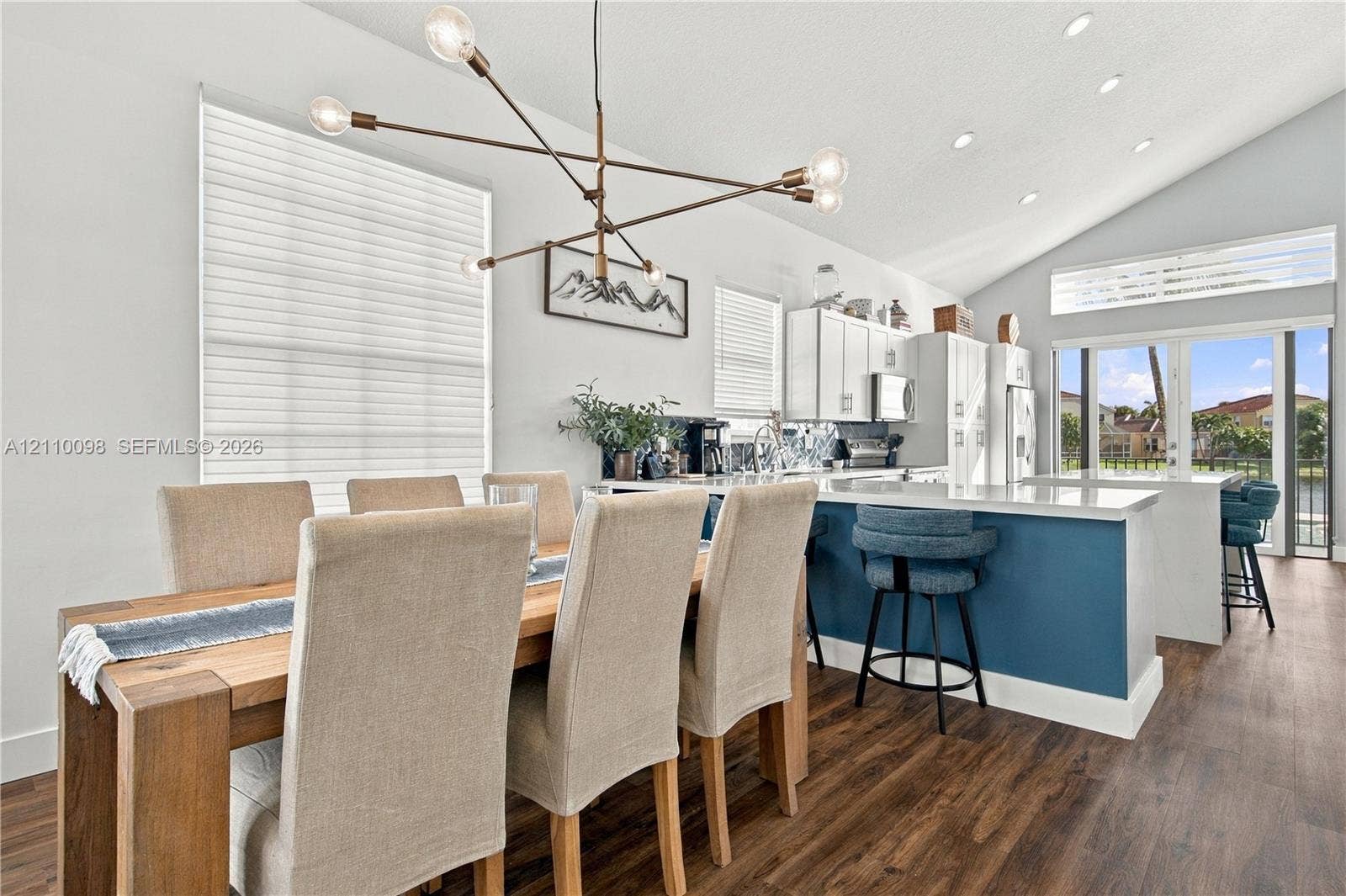 Vaulted ceiling, open-concept kitchen featuring a center island with bar seating, custom white cabinetry, and modern multi-arm chandelier, finished with wood-finish flooring