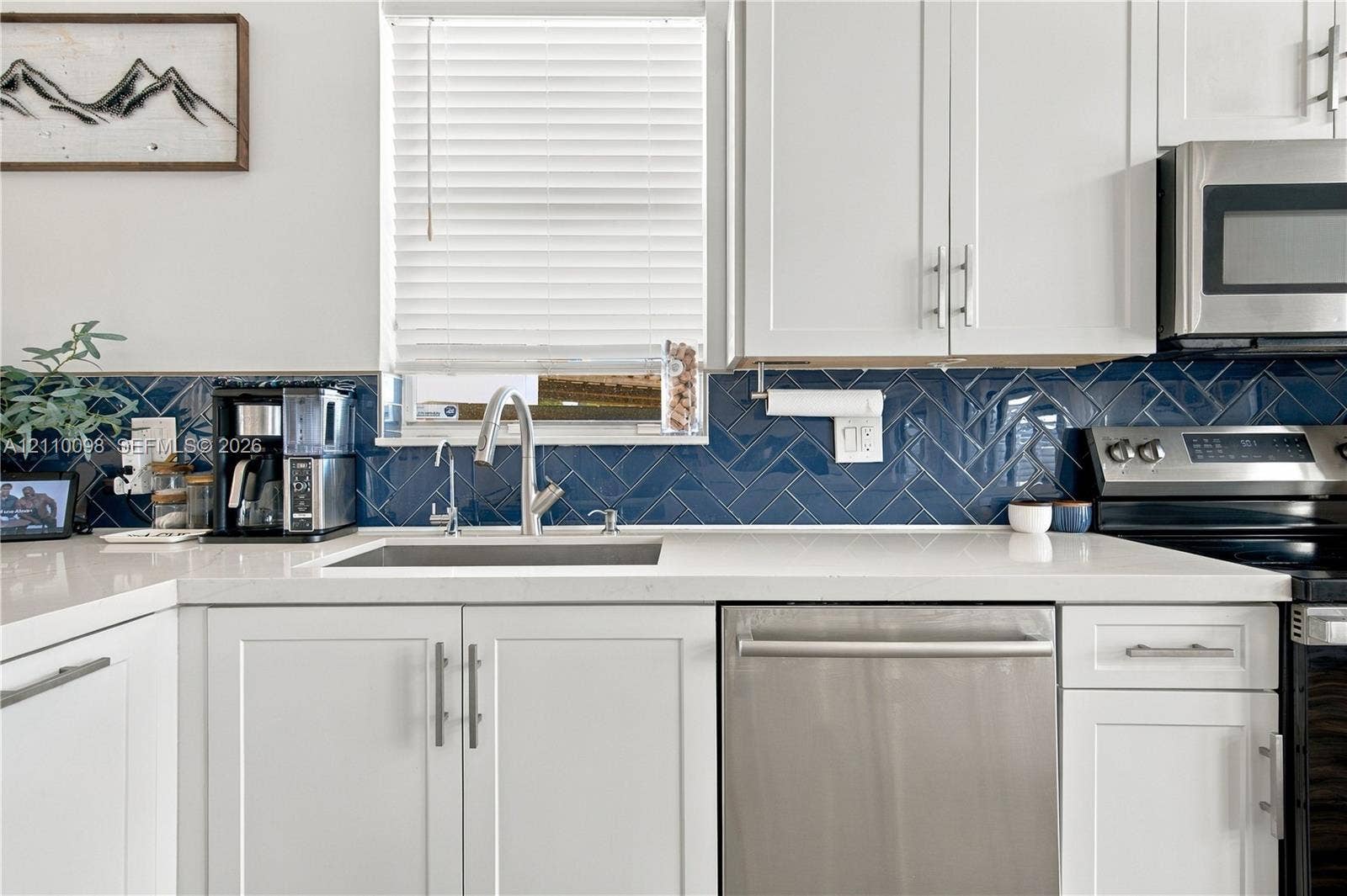 Kitchen featuring white shaker-style cabinetry, quartz countertops, herringbone-patterned tile backsplash, stainless steel appliances, and a polished chrome high-arc faucet
