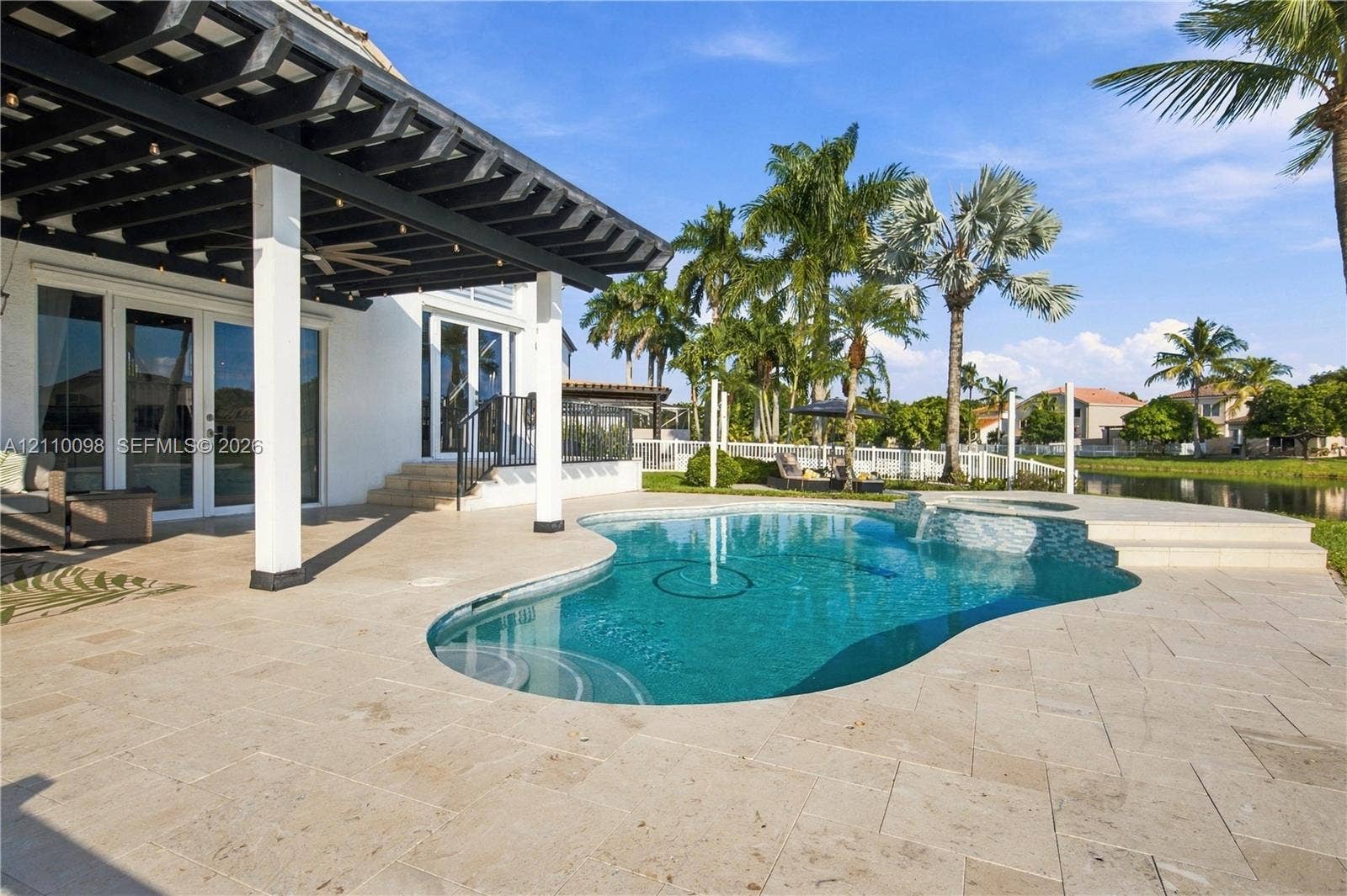 Covered patio featuring a wood-beam pergola, stone-tile decking, freeform swimming pool with a built-in spa, and water frontage