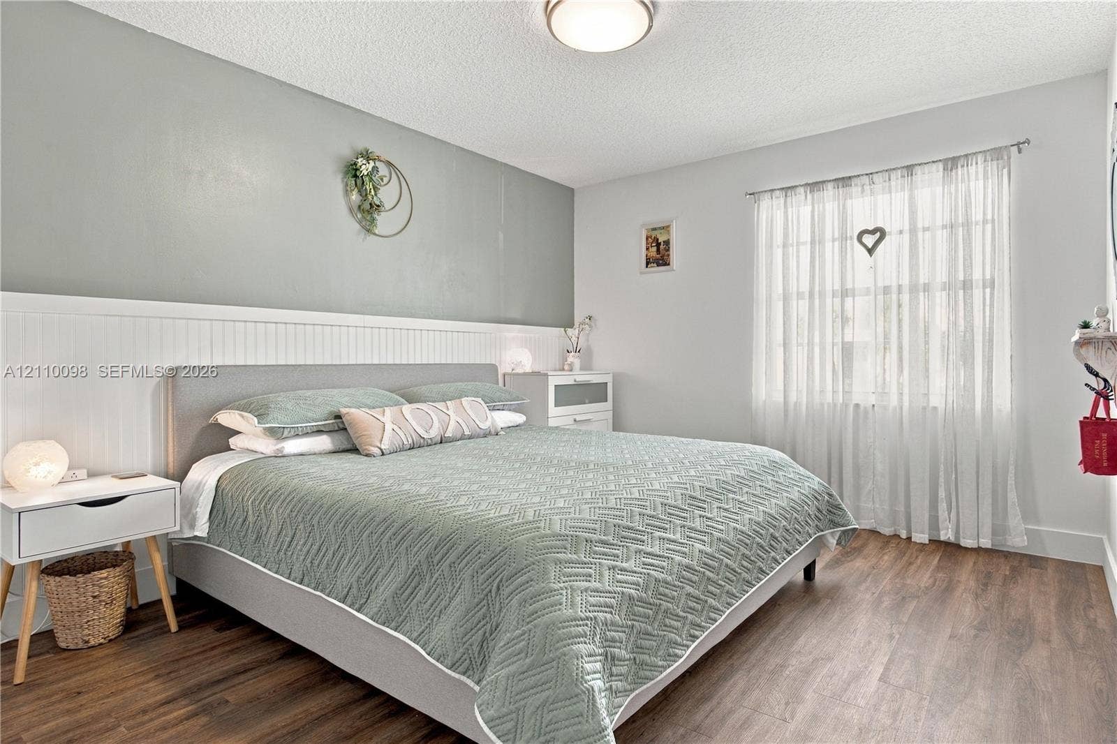 Room featuring wood-finish flooring, white wainscoting, a painted accent wall, and a flush-mount ceiling light fixture