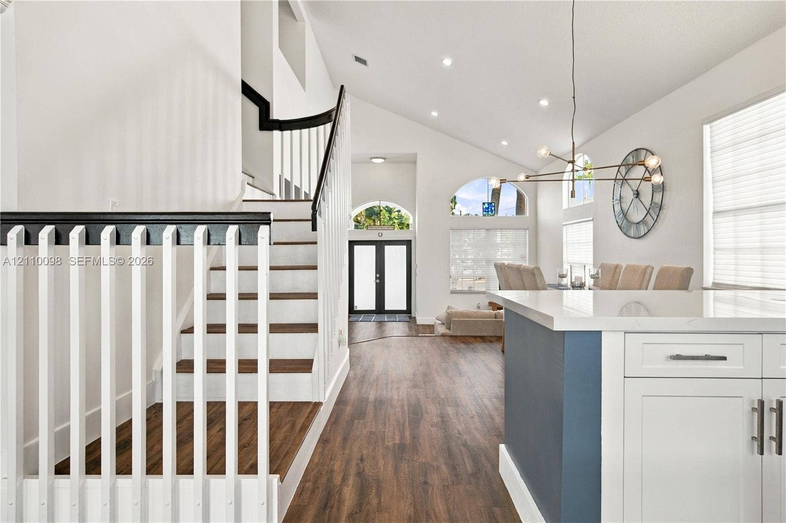 Vaulted ceilings, wood-finish flooring, staircase with contrasting handrail and balusters, architectural arched windows, and kitchen island with white cabinetry