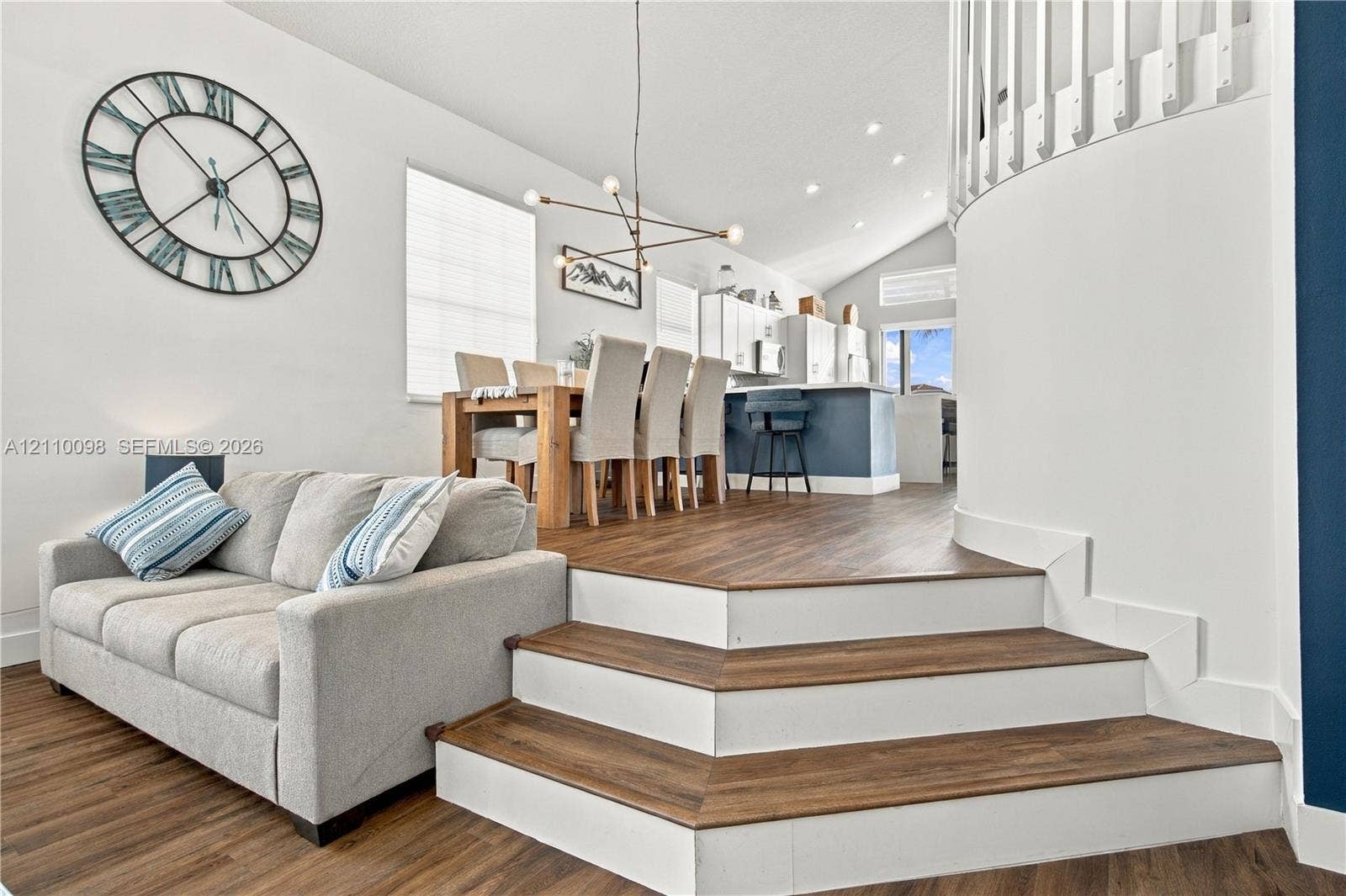 Split-level interior featuring wood-finish flooring, vaulted ceilings, a structural curved staircase with white railing, and multi-arm geometric pendant lighting