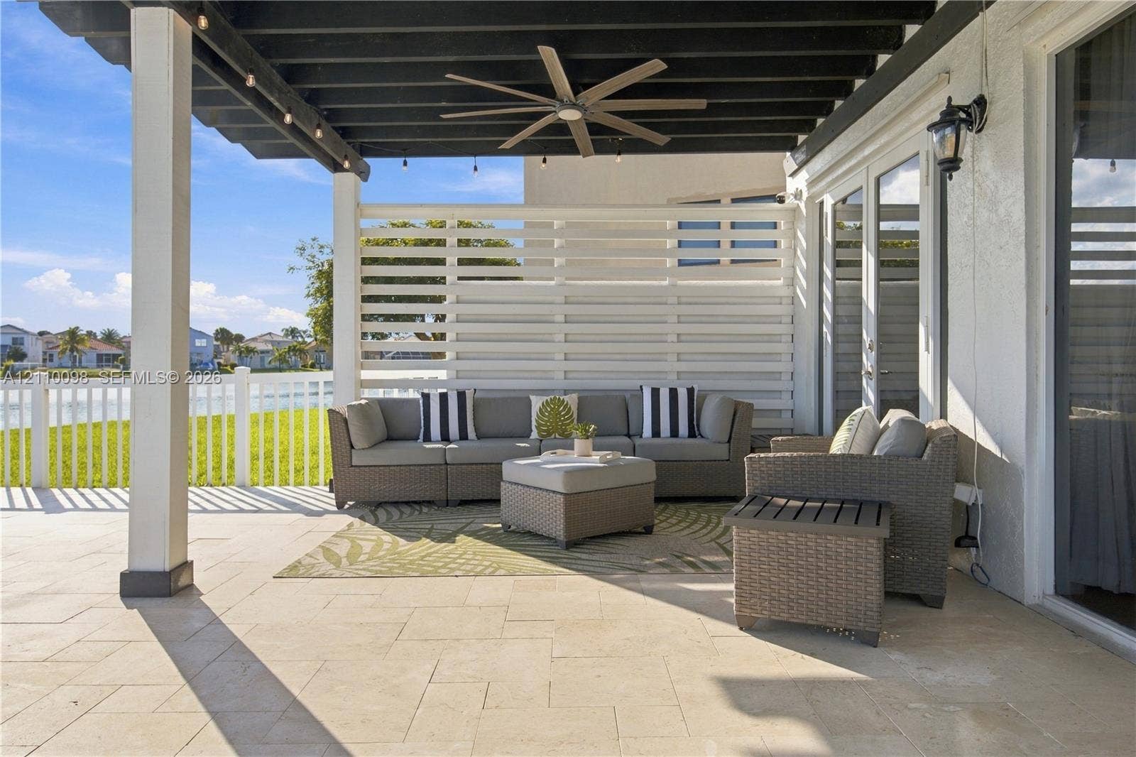 Covered patio featuring stone-tiled flooring, a dark-finished wooden pergola, a ceiling fan, and a white privacy screen