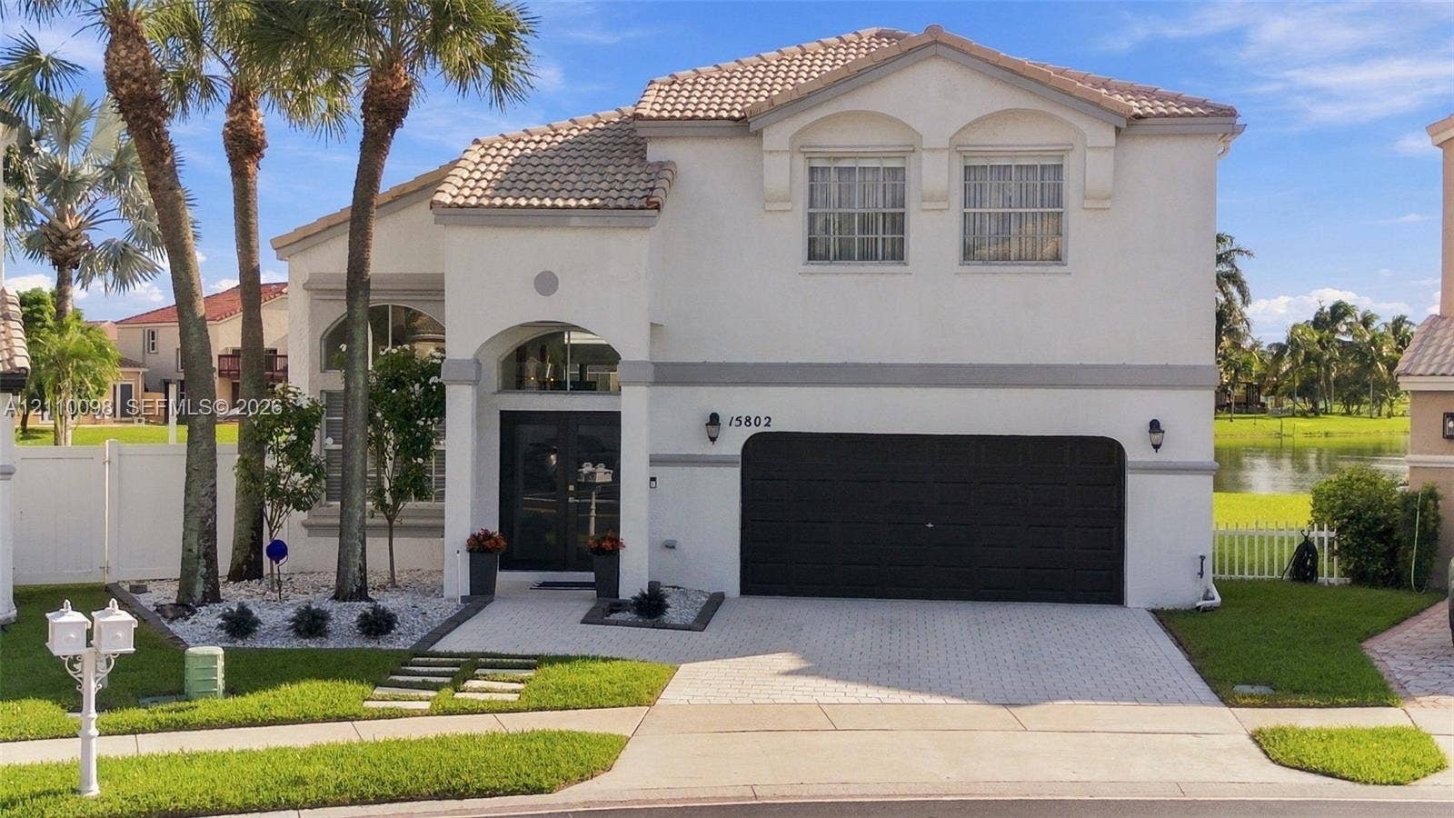Two-story residence featuring a tile roof, arched entryway, paved driveway, multi-car garage, and waterfront surroundings