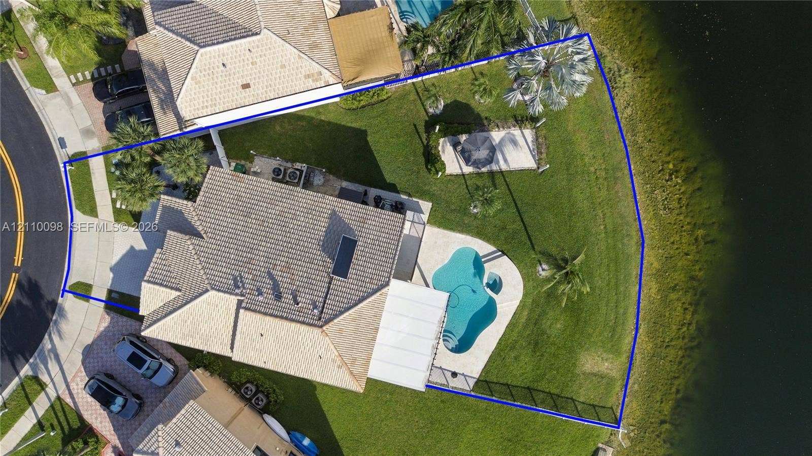 Aerial view of a waterfront property featuring a paved swimming pool deck, a private pool, a concrete patio area, and expansive lawn space