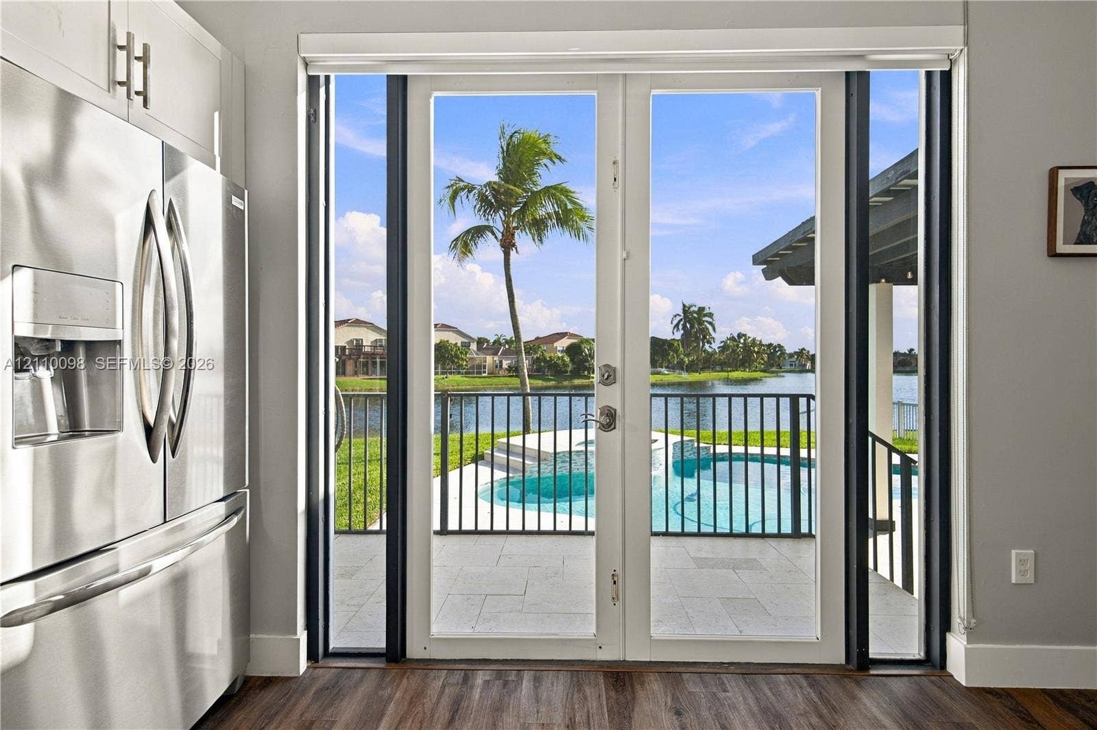 Stainless steel refrigerator, glass-paned double doors, patio with stone-finish pavers, private swimming pool, and water-facing iron fencing