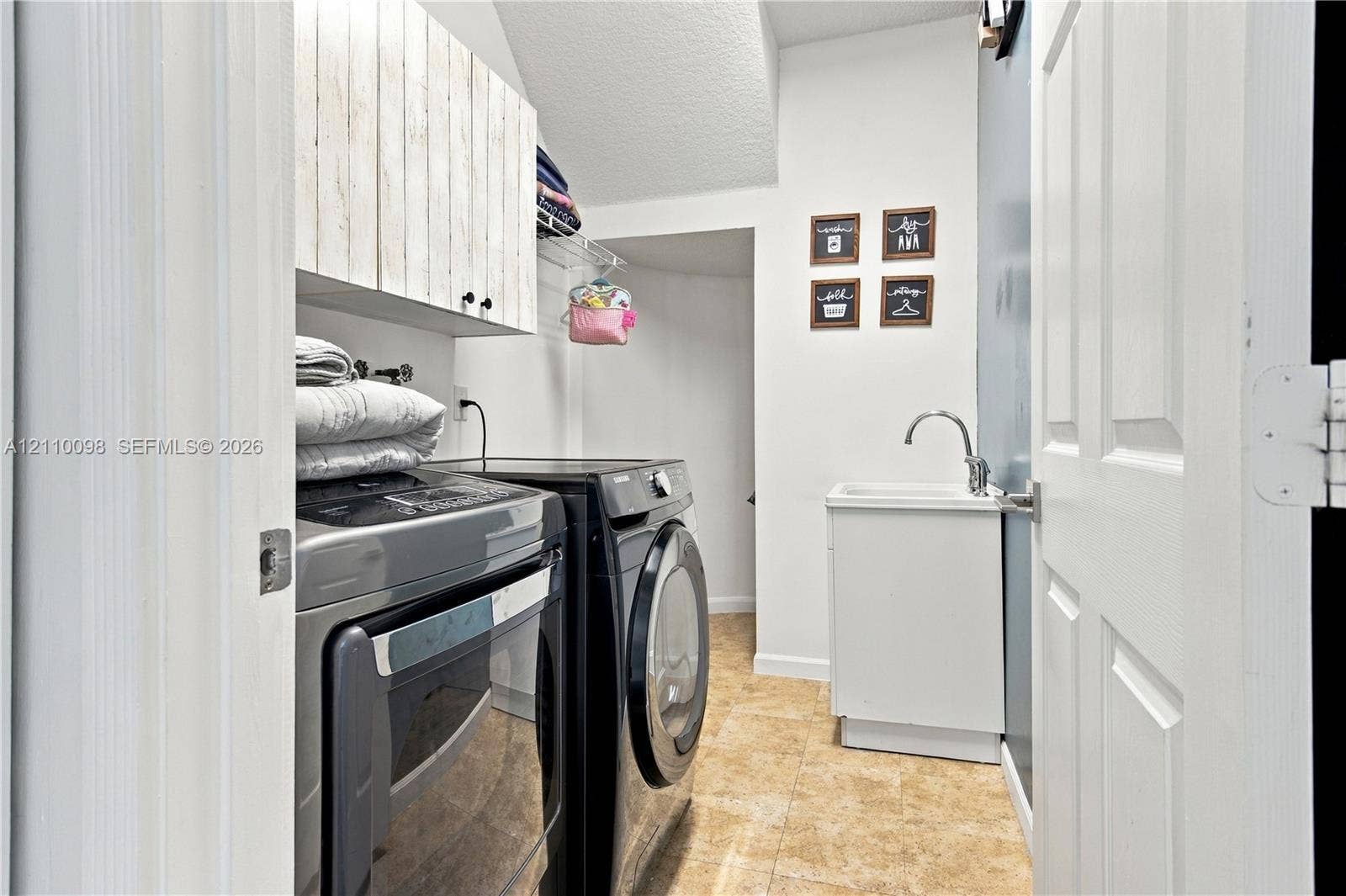 Laundry area featuring vertical wood-plank cabinetry, a utility sink with a gooseneck faucet, wire shelving, and neutral tile flooring